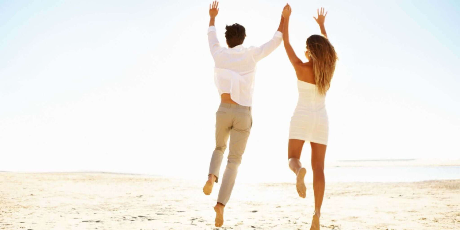 Happy couple running hand-in-hand on a sunny beach, symbolizing the benefits of boosting libido naturally with Sacred Plant Co's herbal remedies.