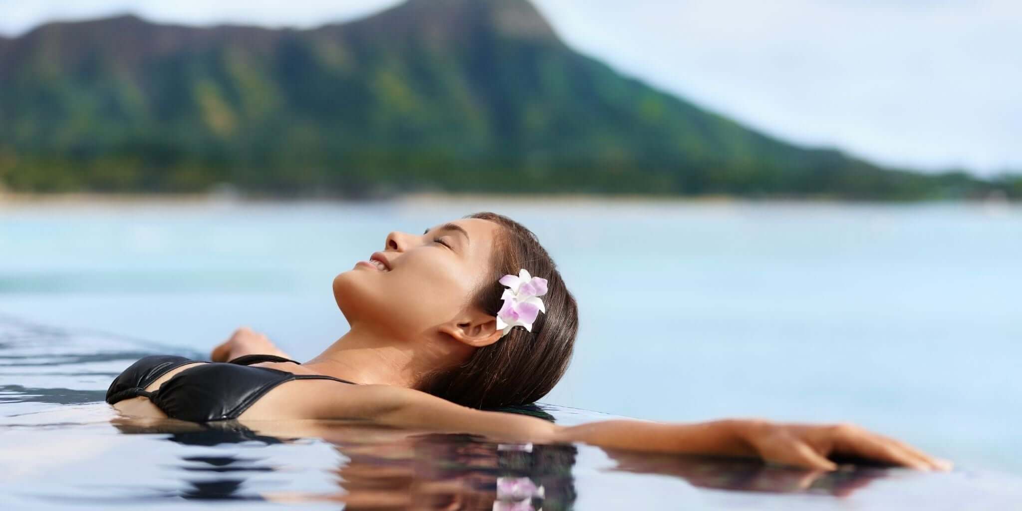 This image features a serene scene of a person relaxing in a pool with a tranquil backdrop of mountains and water.
