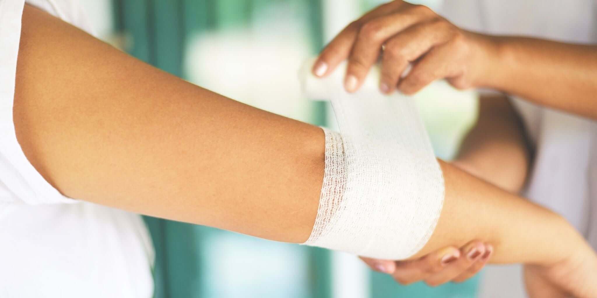 The image features a close-up of a healthcare professional gently wrapping a bandage around an arm, symbolizing care and healing.