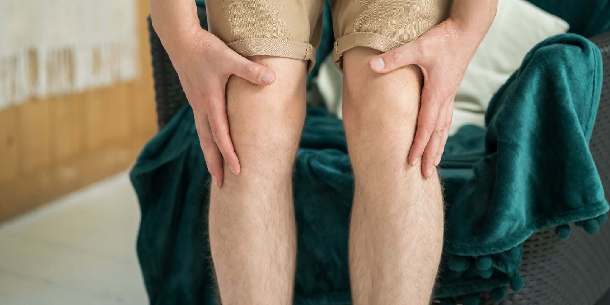 A close-up image of a person sitting on a comfortable chair, hands gently massaging their knees.