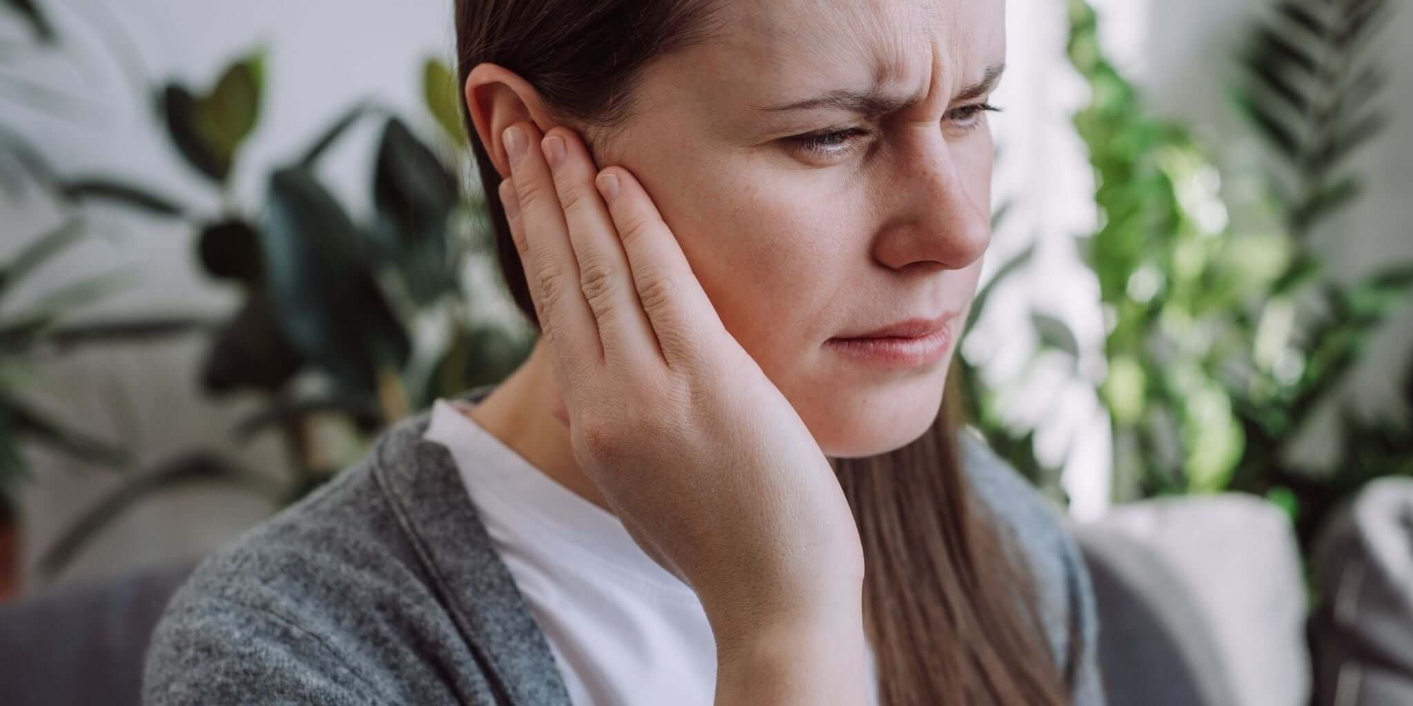 A woman holds her hand to her ear with a pained expression, suggesting discomfort or tinnitus.