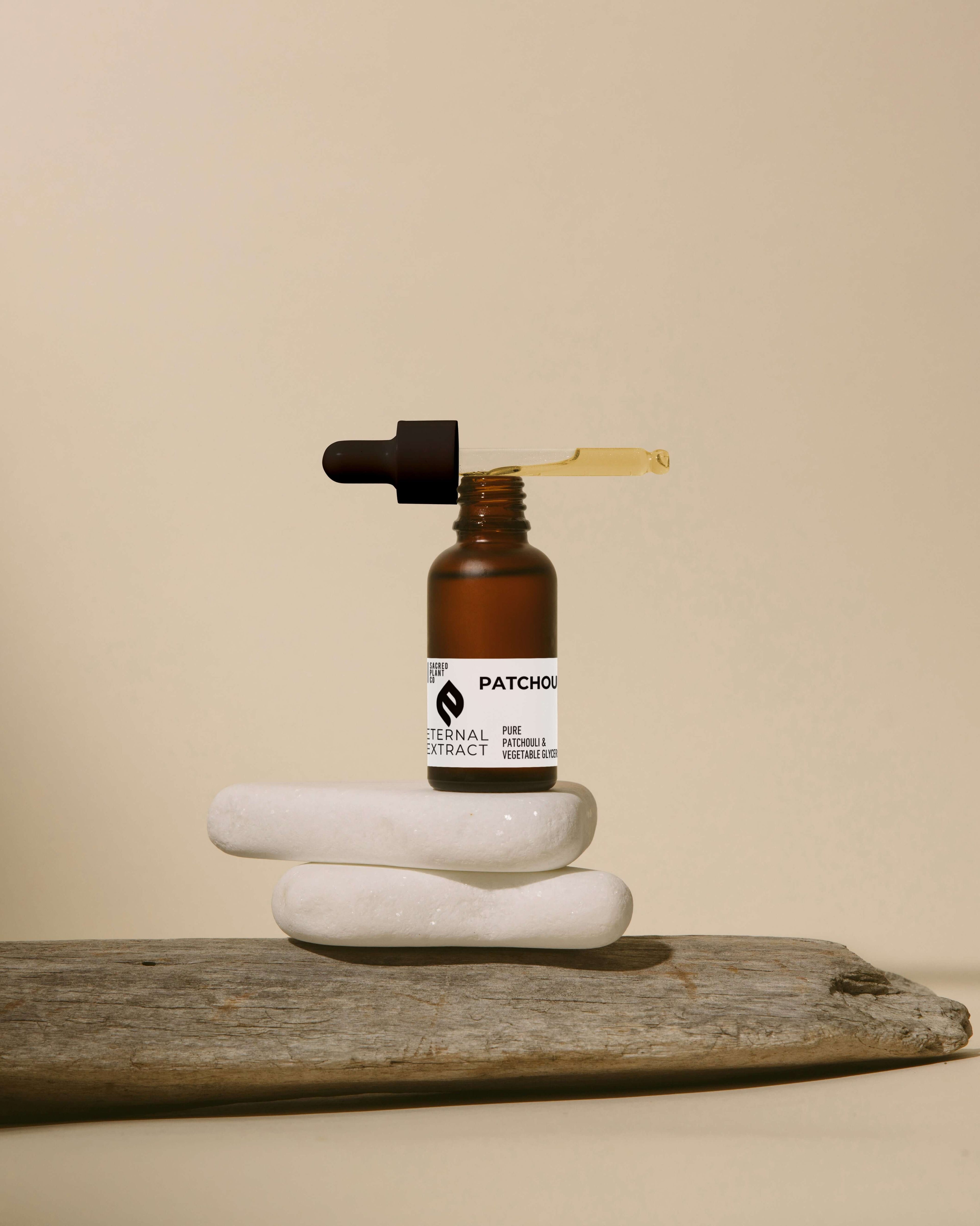 Artistic display of Sacred Plant Co Eternal Patchouli Extract, a natural skincare essential, on zen-like stones against a neutral background.