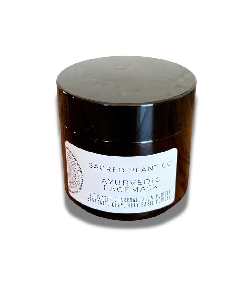 A black jar of Sacred Plant Co Ayurvedic Facemask, featuring a white label listing key ingredients like activated charcoal, neem powder, bentonite clay, and holy basil powder.