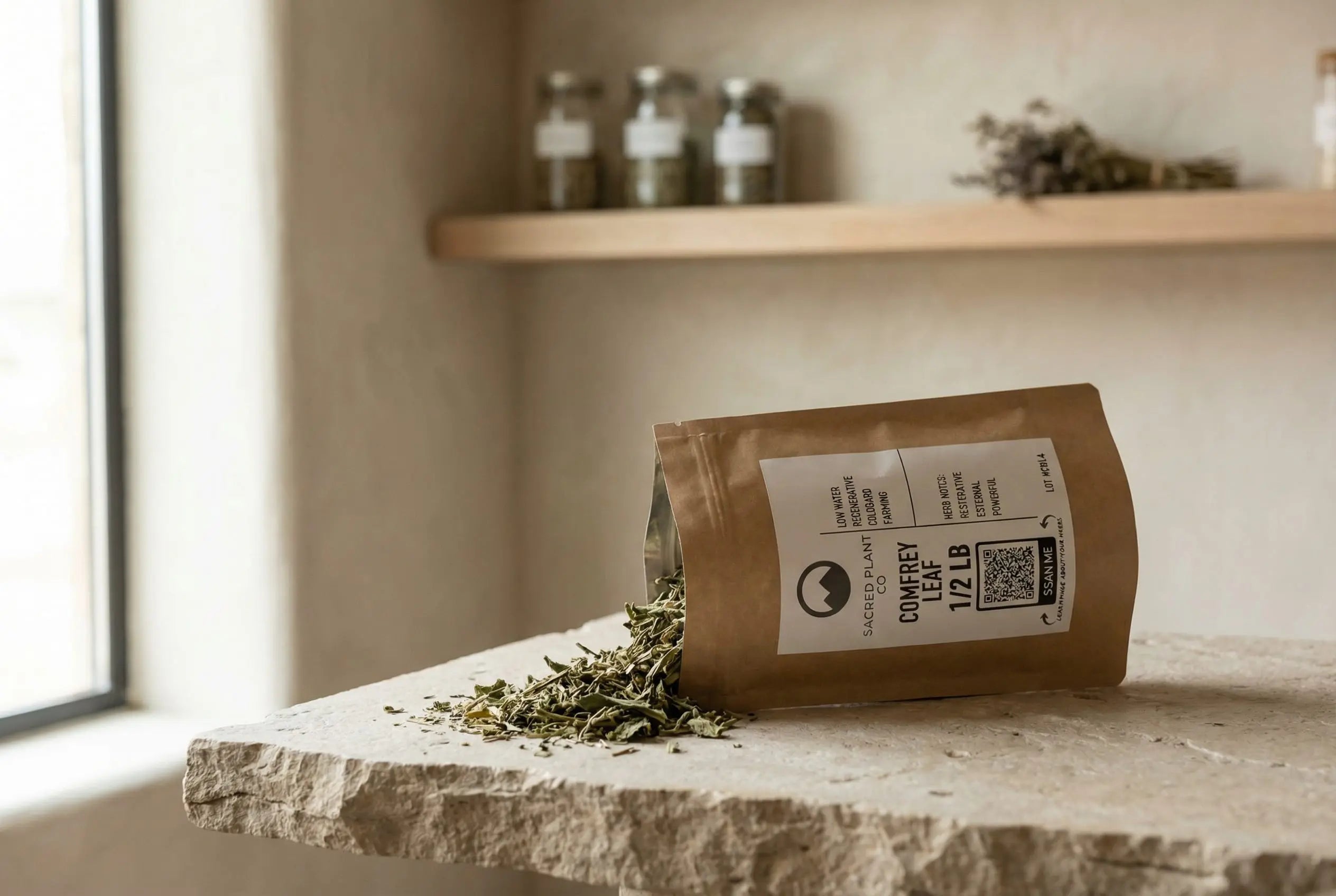 Comfrey leaf spilling out os Sacred Plant Co bag on stone tablet, in apothecary.