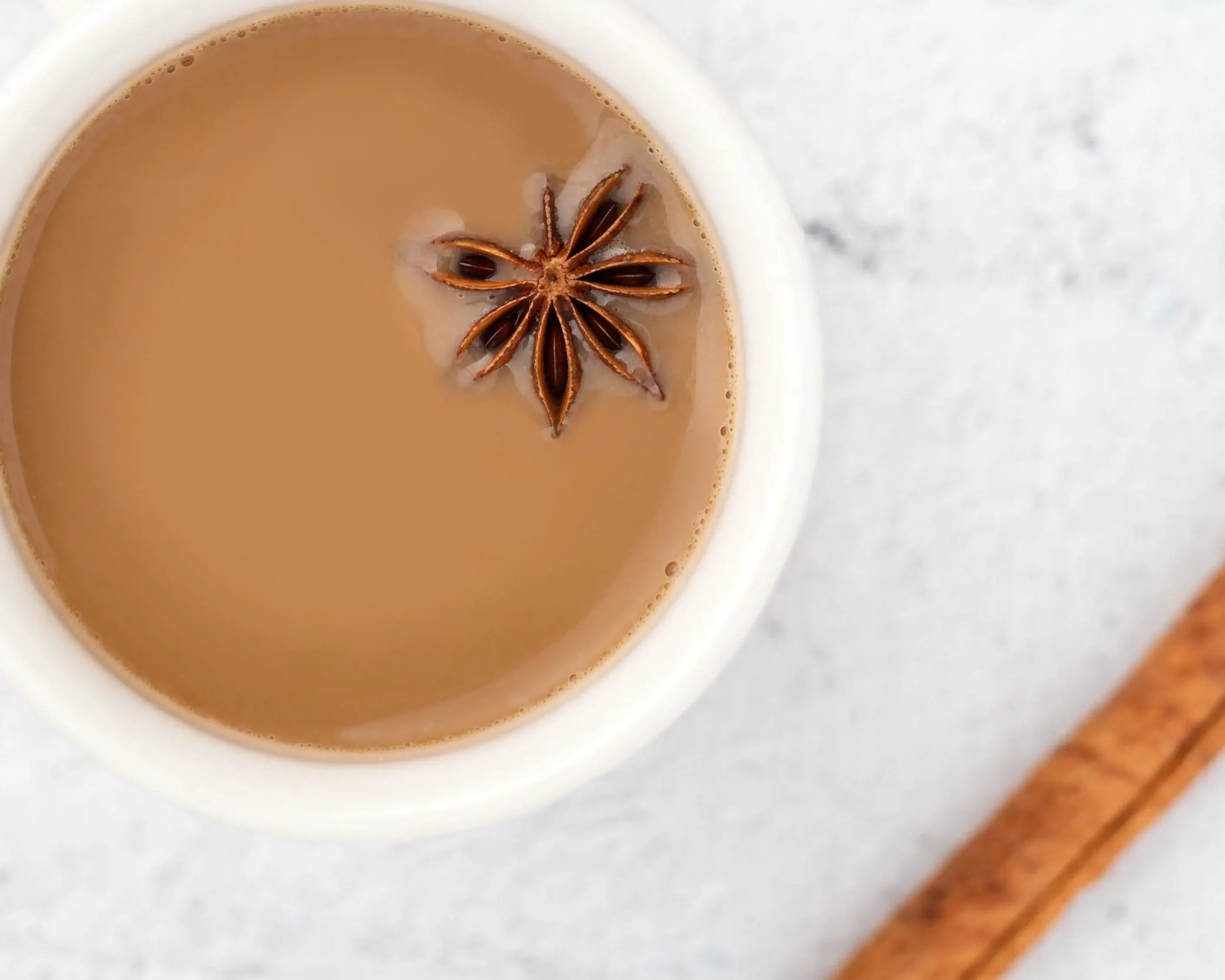 Cup of Sacred Plant Co Tulsi Chai Tea with star anise, showcasing aromatic herbs, set against a light background, top view, creamy color, and glossy ceramic texture.