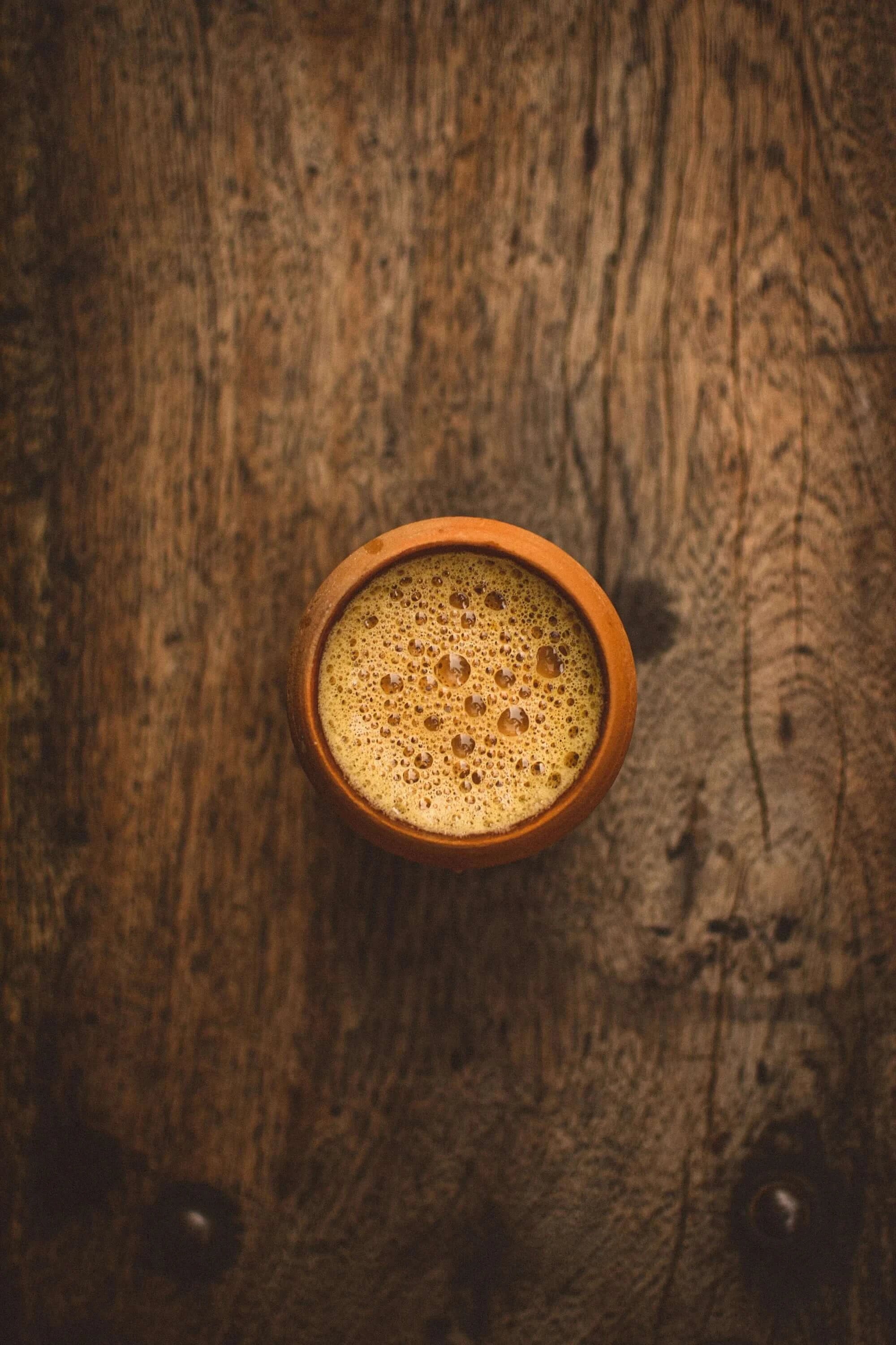 Top view of Sacred Plant Co Tulsi Chai Tea in a clay cup on a wooden background, showcasing herb quality, natural simplicity, warm tones, and a rough wood texture.