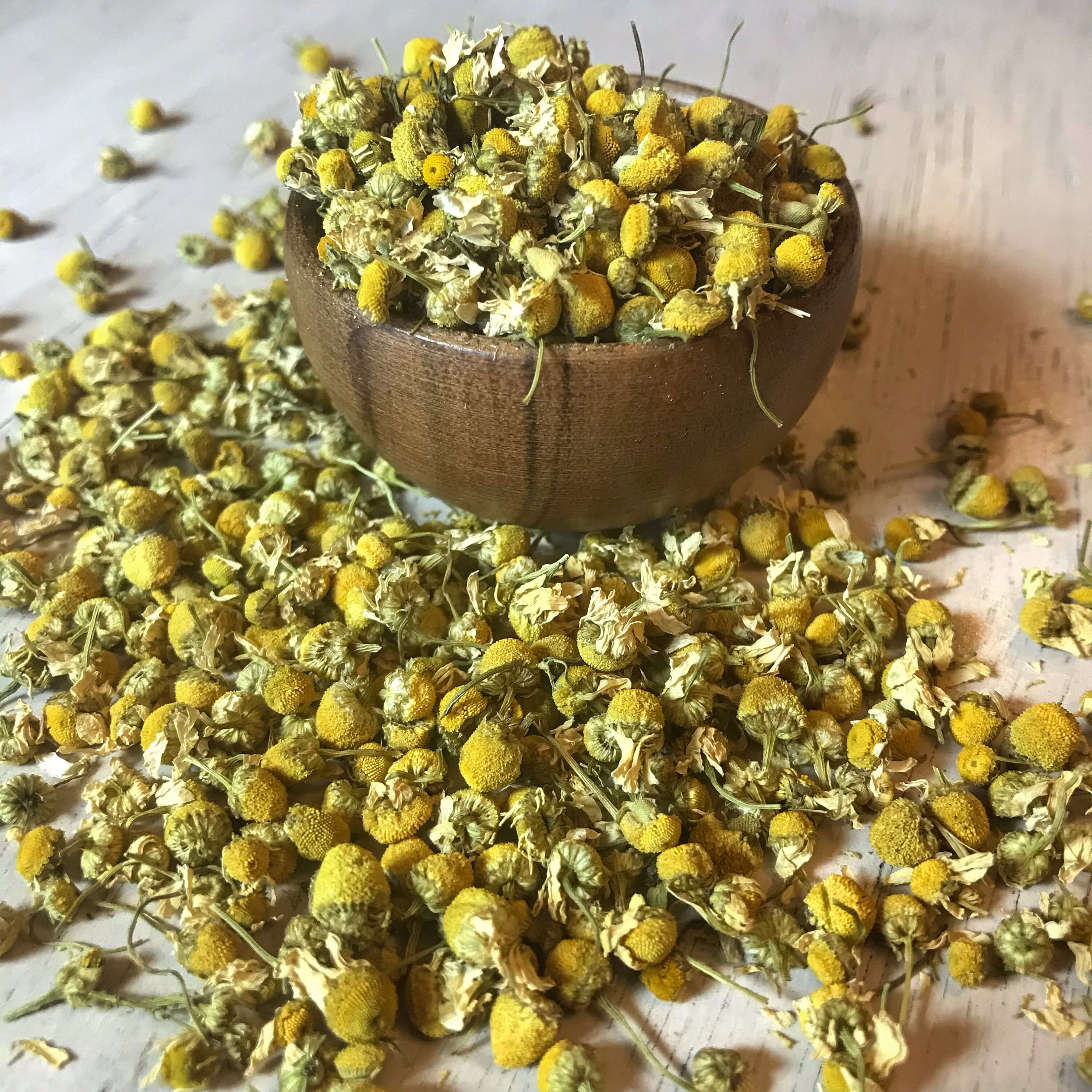 Organic dried chamomile flowers spilling from a natural wooden bowl onto a rustic surface, highlighting the premium quality for teas and aromatherapy