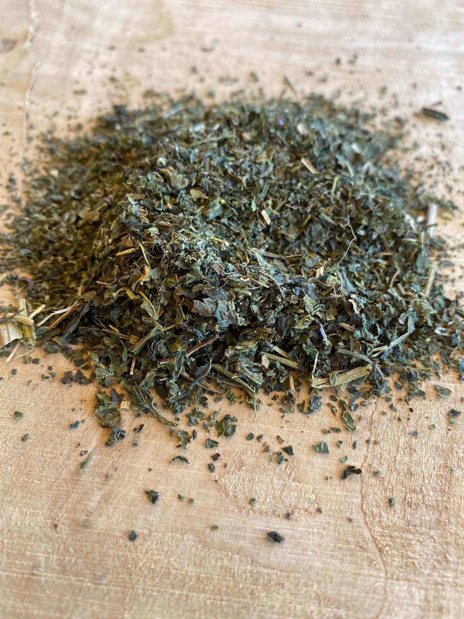 Dried Stinging Nettle Leaf, ethically sourced and cultivated through innovative regenerative agriculture. This premium green herb is prized for its natural support of joint health, seasonal allergies, and overall vitality. Displayed loose on a rustic wood surface, the finely cut texture highlights its freshness and botanical integrity.
