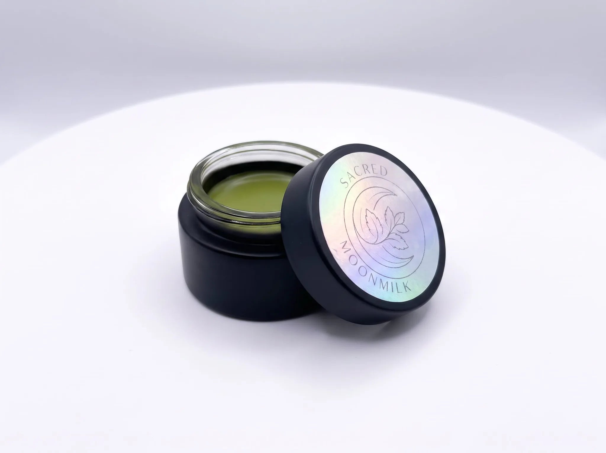 Open jar of Moonmilk Botanical Night Balm with holographic freshness seal, showing the small-batch golden balm