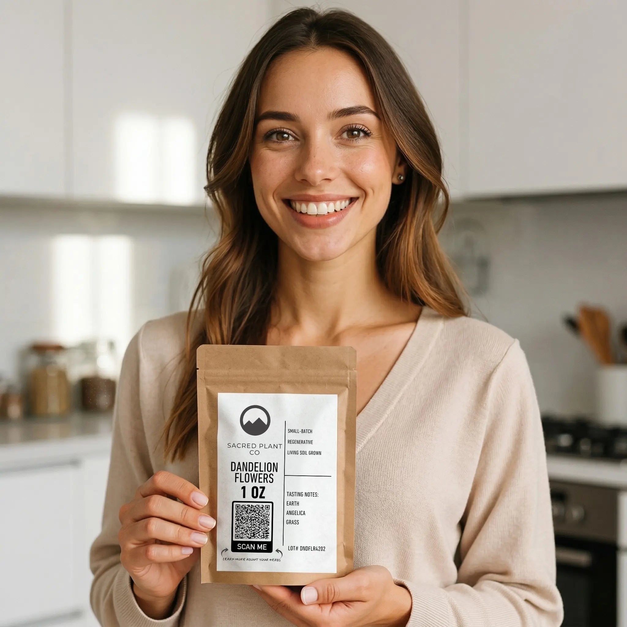 A smiling woman in a bright kitchen holding a kraft paper stand-up pouch of Sacred Plant Co&