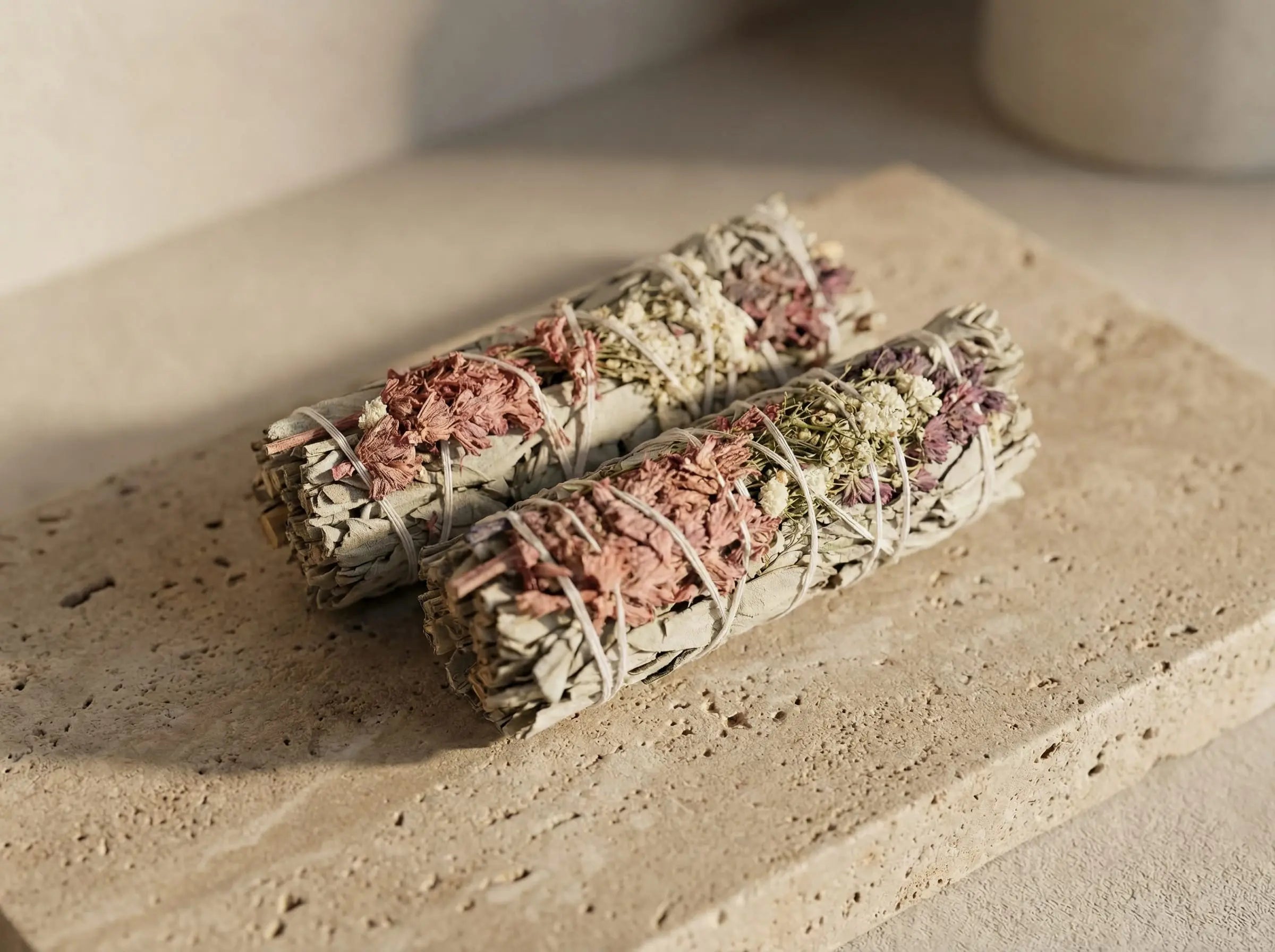 White sage smudge sticks photographed on textured natural stone, highlighting leaf structure and hand-tied form.