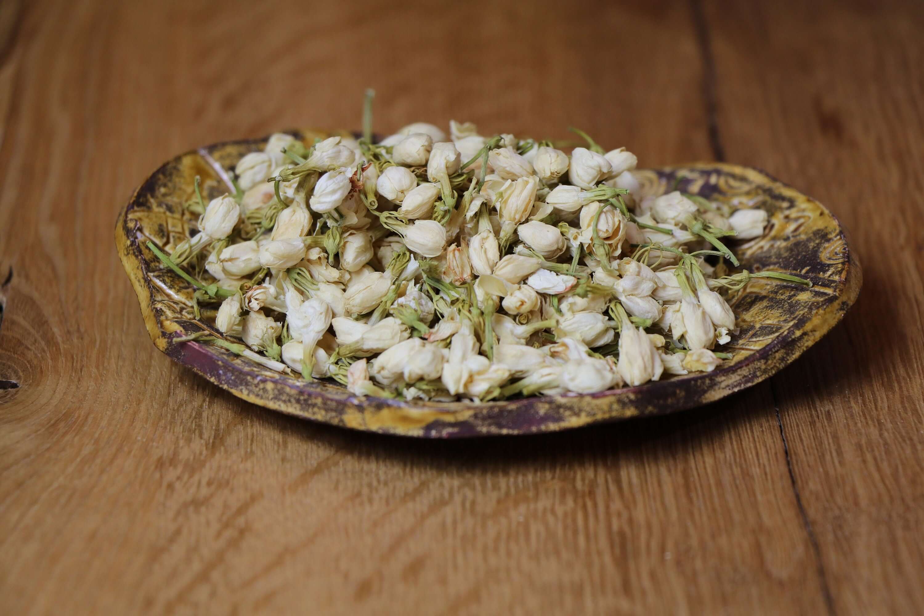 Organic Jasmine Flowers resting on a handcrafted ceramic plate, representing the high quality and purity of Sacred Plant Co’s herbs.