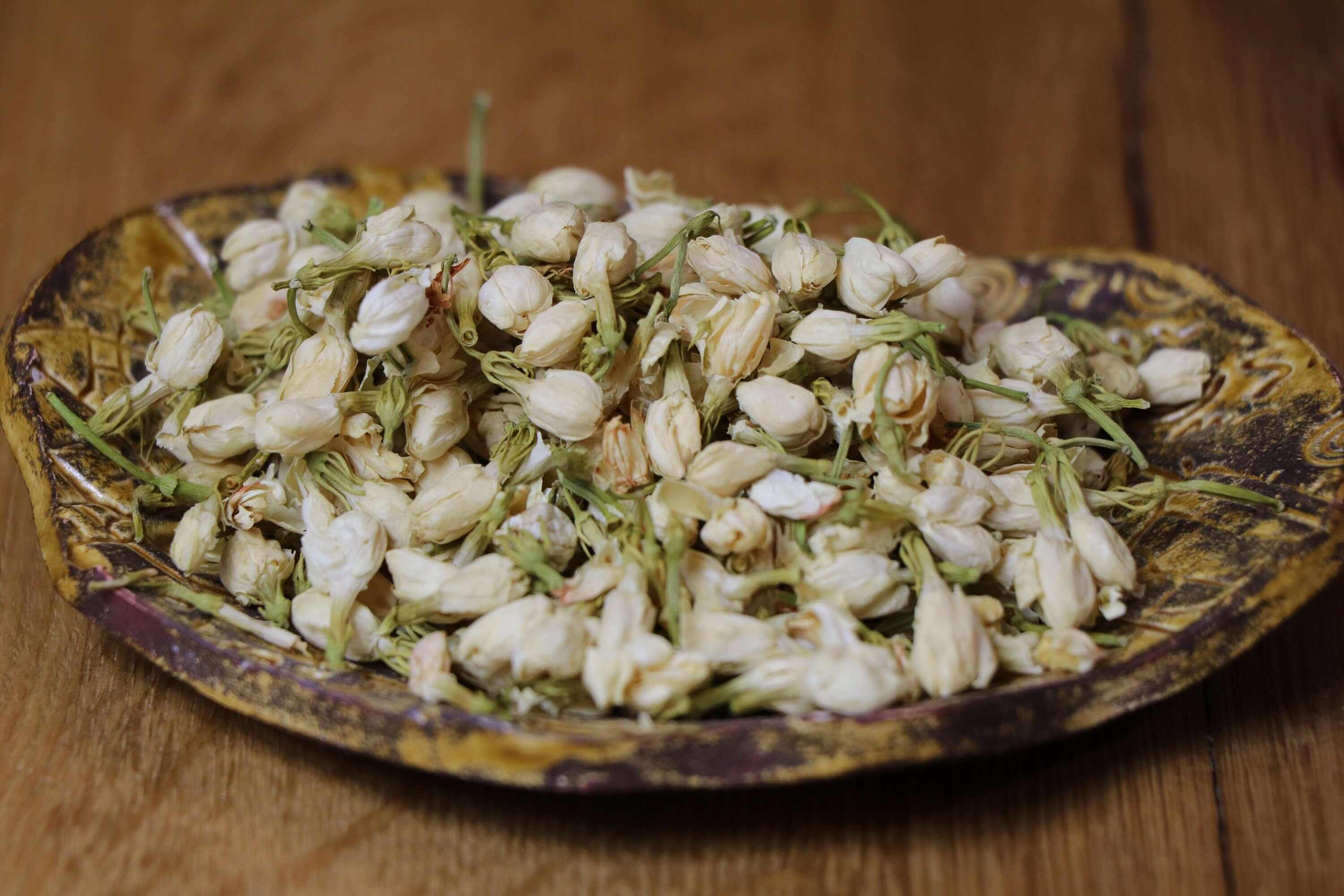 Dried Jasmine Flowers on a rustic dish over a wooden surface, capturing the natural texture and premium quality of Sacred Plant Co.