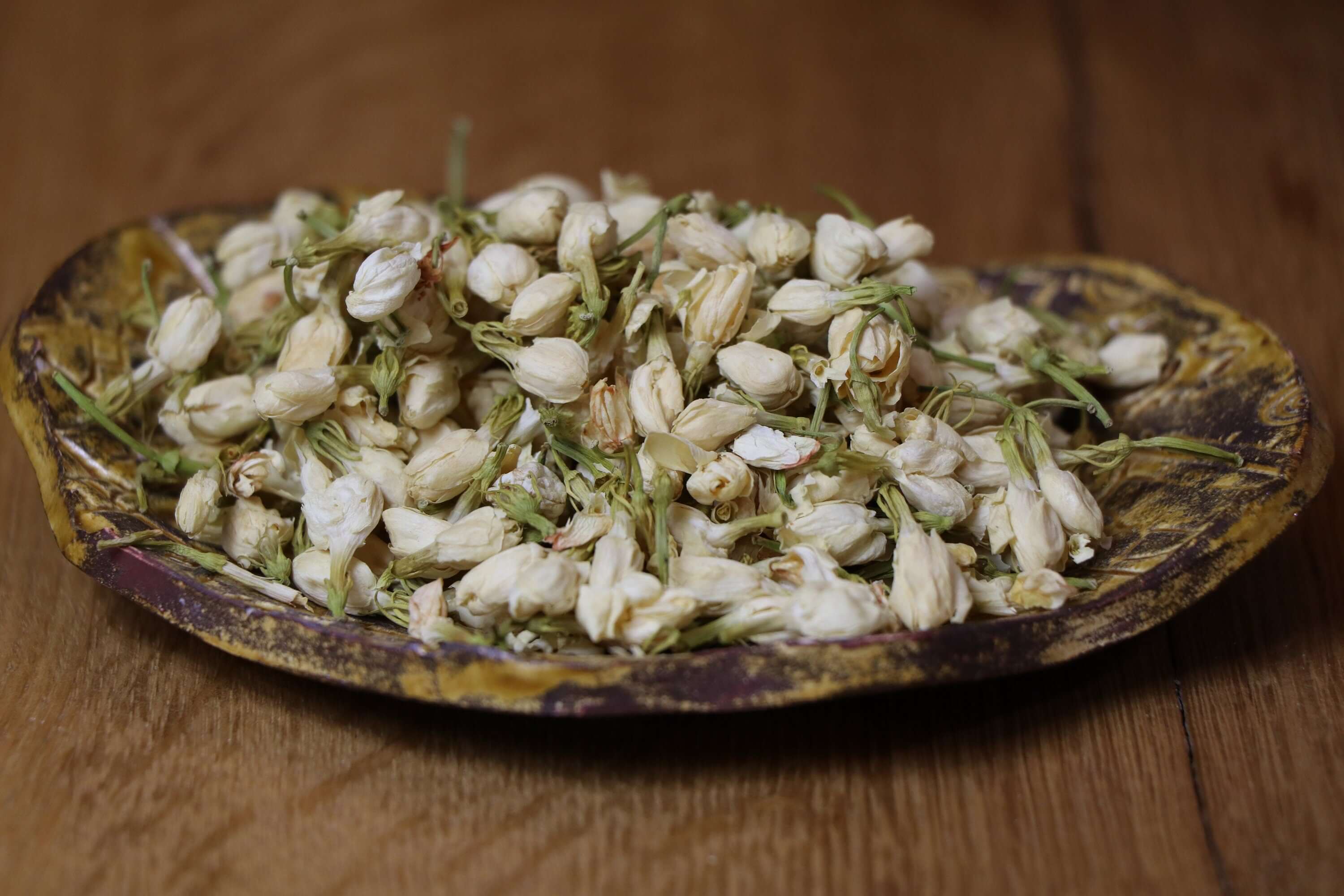 Premium dried Jasmine Flowers arranged on a rustic plate with a wood background, showcasing Sacred Plant Co’s sustainable herbs.