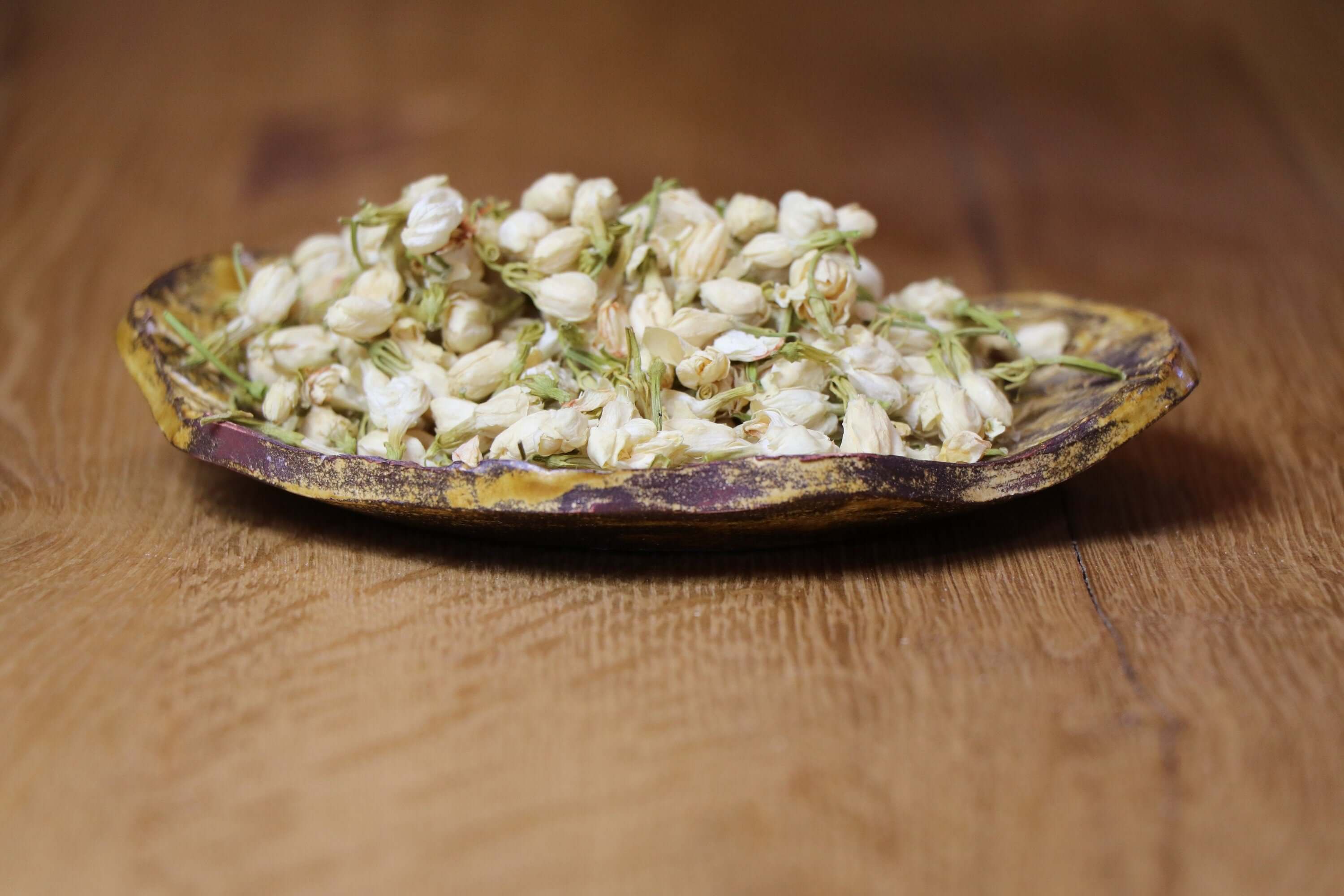 Dried Jasmine Flowers displayed on a rustic ceramic plate, highlighting the premium quality of Sacred Plant Co’s herbs.