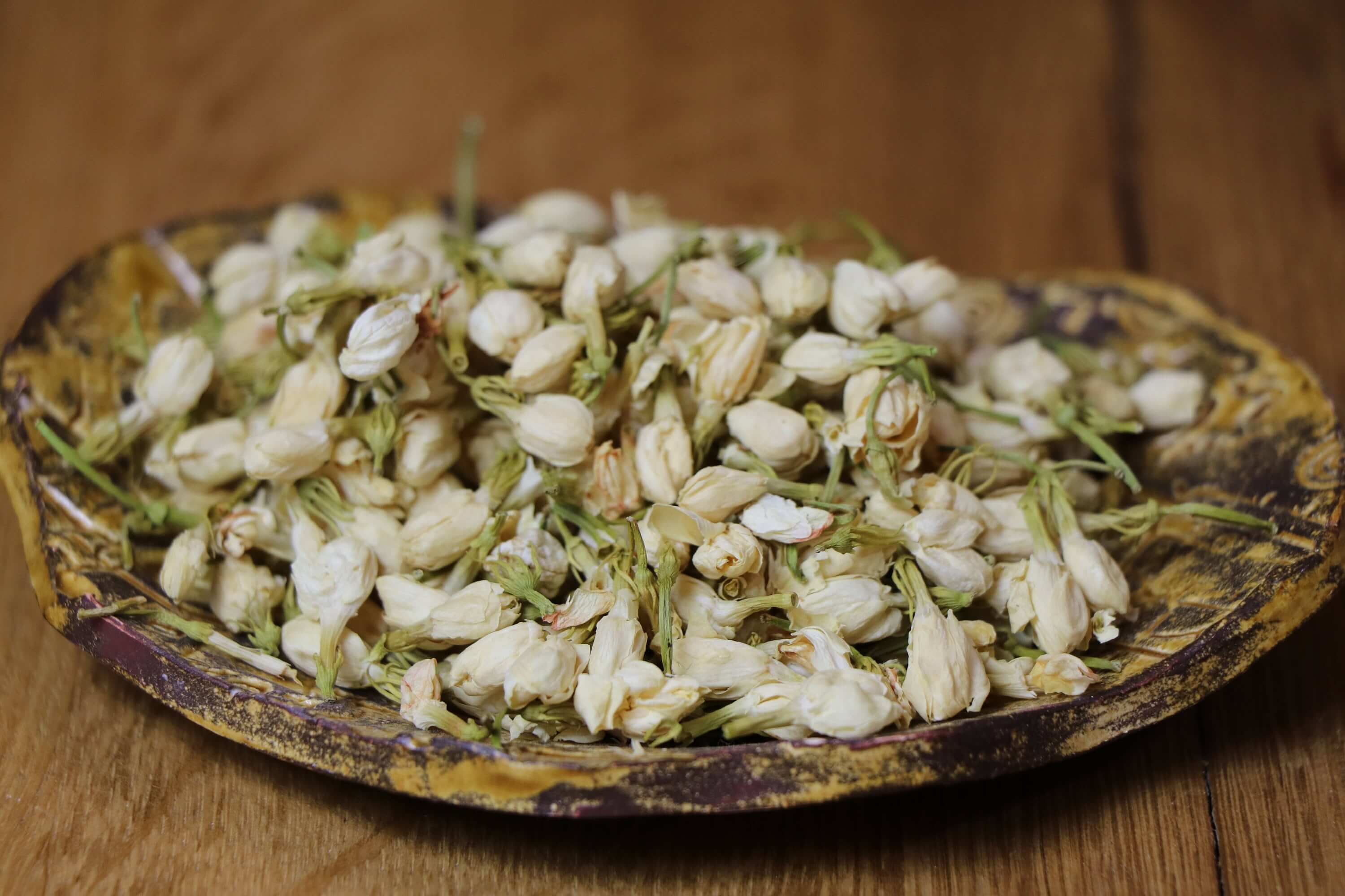 Handpicked dried Jasmine Flowers on a rustic ceramic dish, showcasing the rich texture and premium quality of Sacred Plant Co’s herbs.