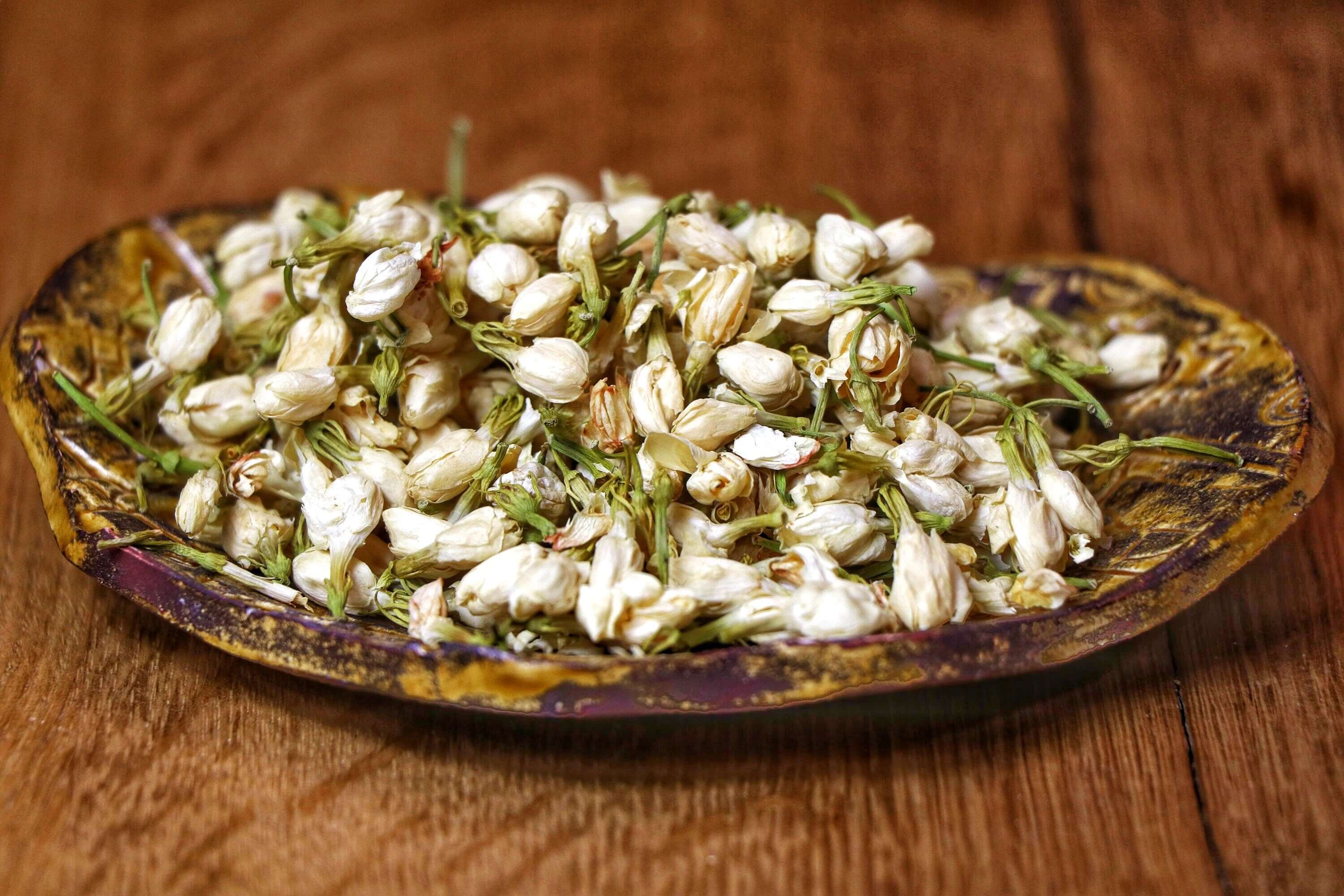 Freshly harvested dried Jasmine Flowers on a handcrafted ceramic dish, emphasizing the natural texture and quality.