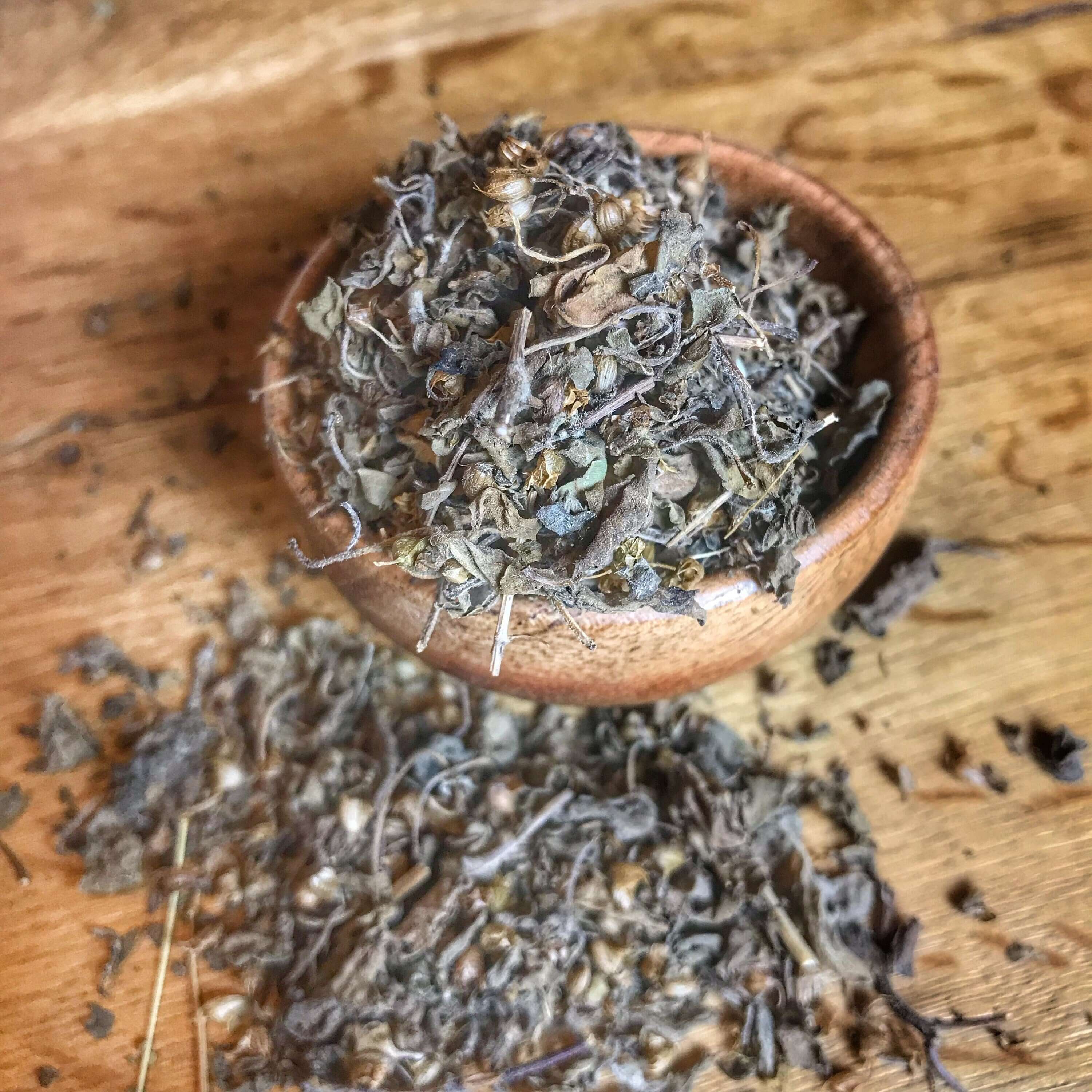 Sacred Plant Co dried Tulsi Herb in a wooden bowl with scattered leaves on a rustic wooden background, showcasing its premium texture.
