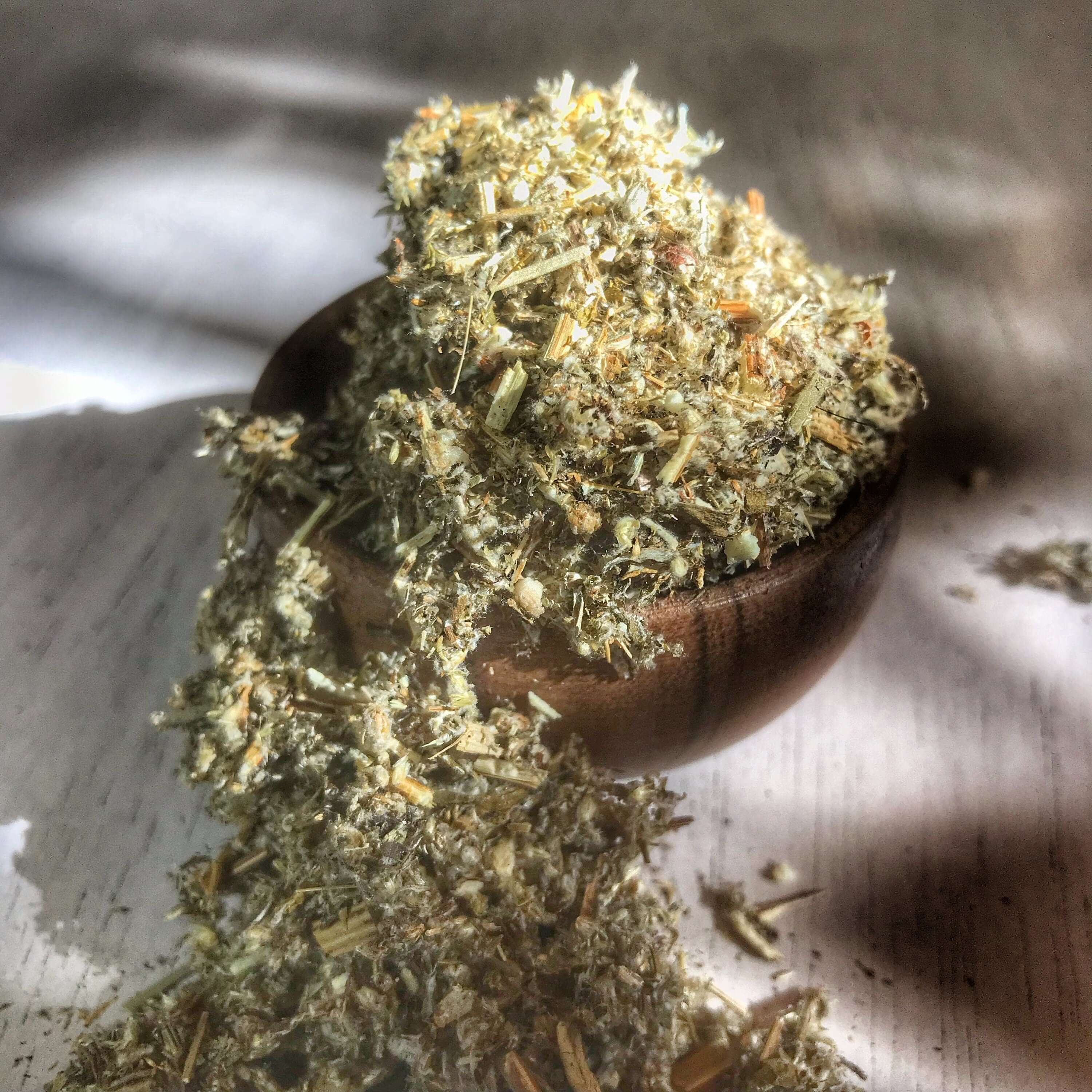 Mugwort Herb scattered from a wooden bowl, highlighting its fine texture and natural tones, symbolizing Sacred Plant Co&