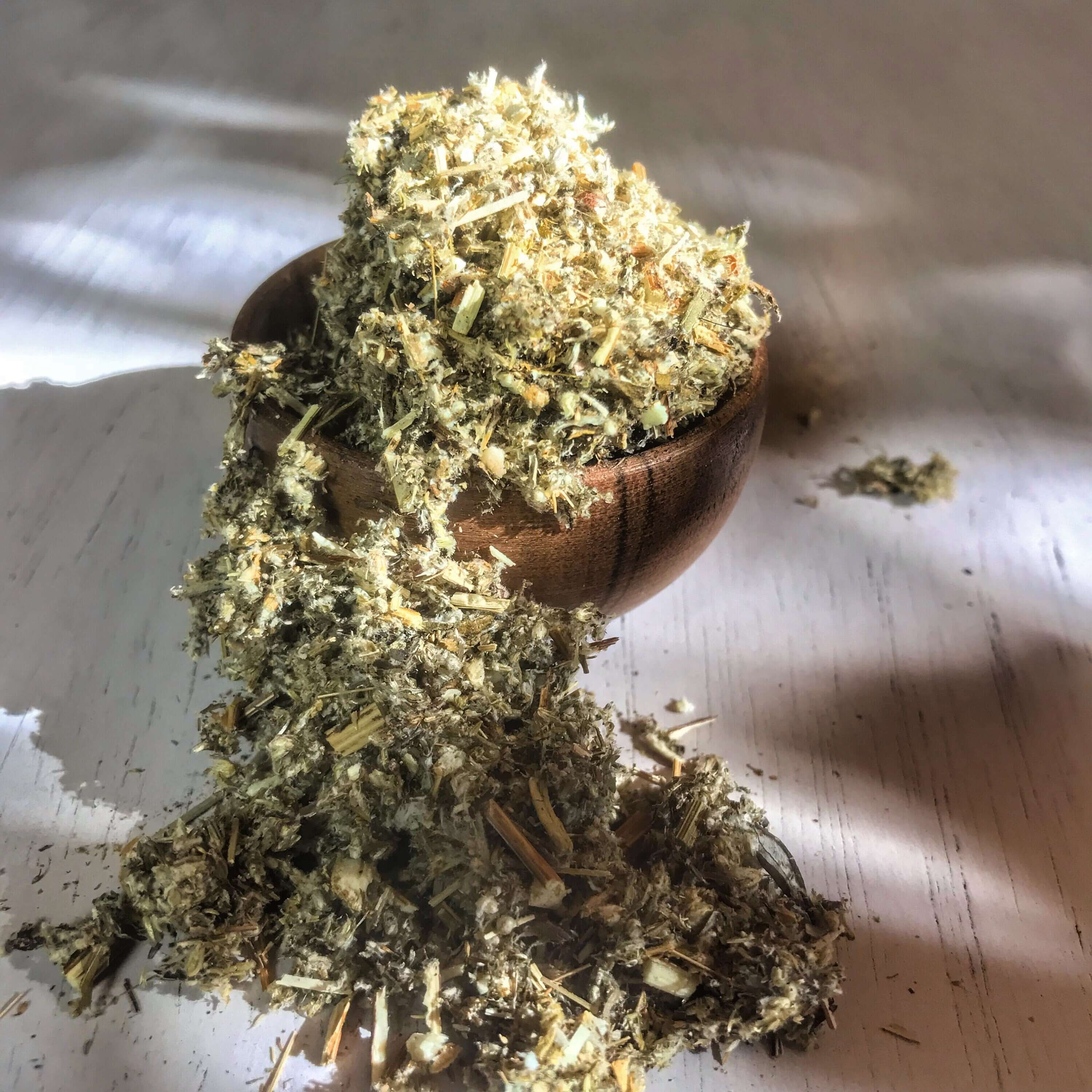 Loose Mugwort Herb flowing from a wooden bowl, showcasing its earthy texture, premium quality, and natural appeal from Sacred Plant Co.
