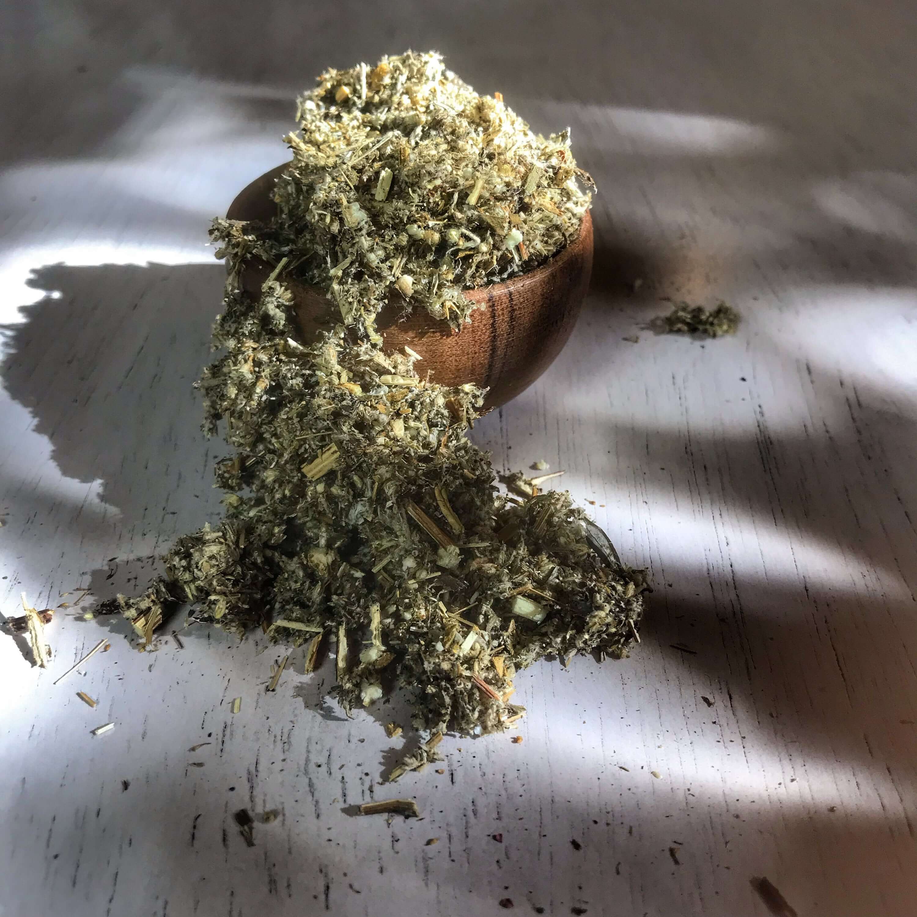Dried Mugwort Herb cascading out of a wooden bowl, emphasizing the herb&