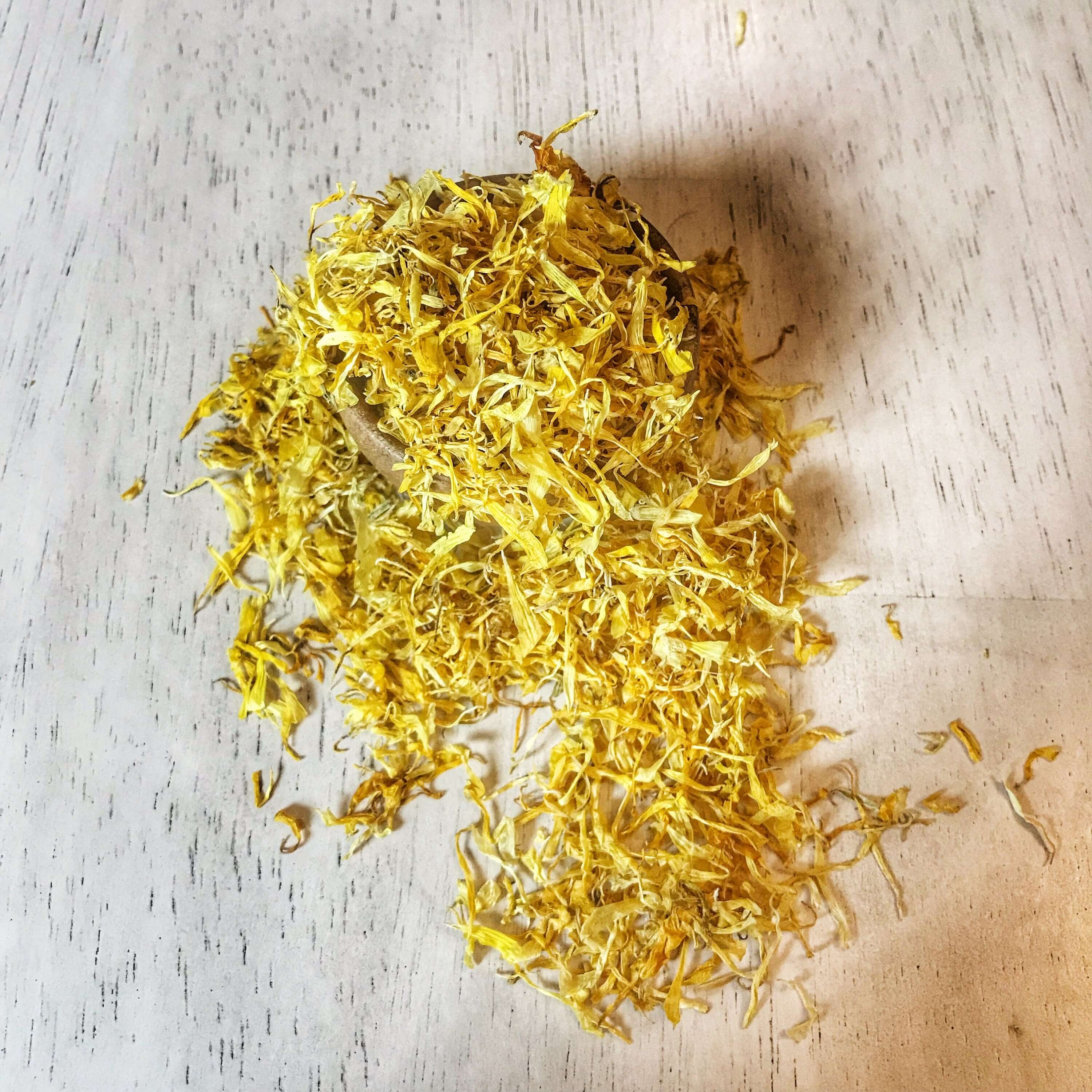 Angled shot of Sacred Plant Co dried Calendula Petals spilling from a wooden bowl, highlighting the high-quality vibrant yellow flowers.