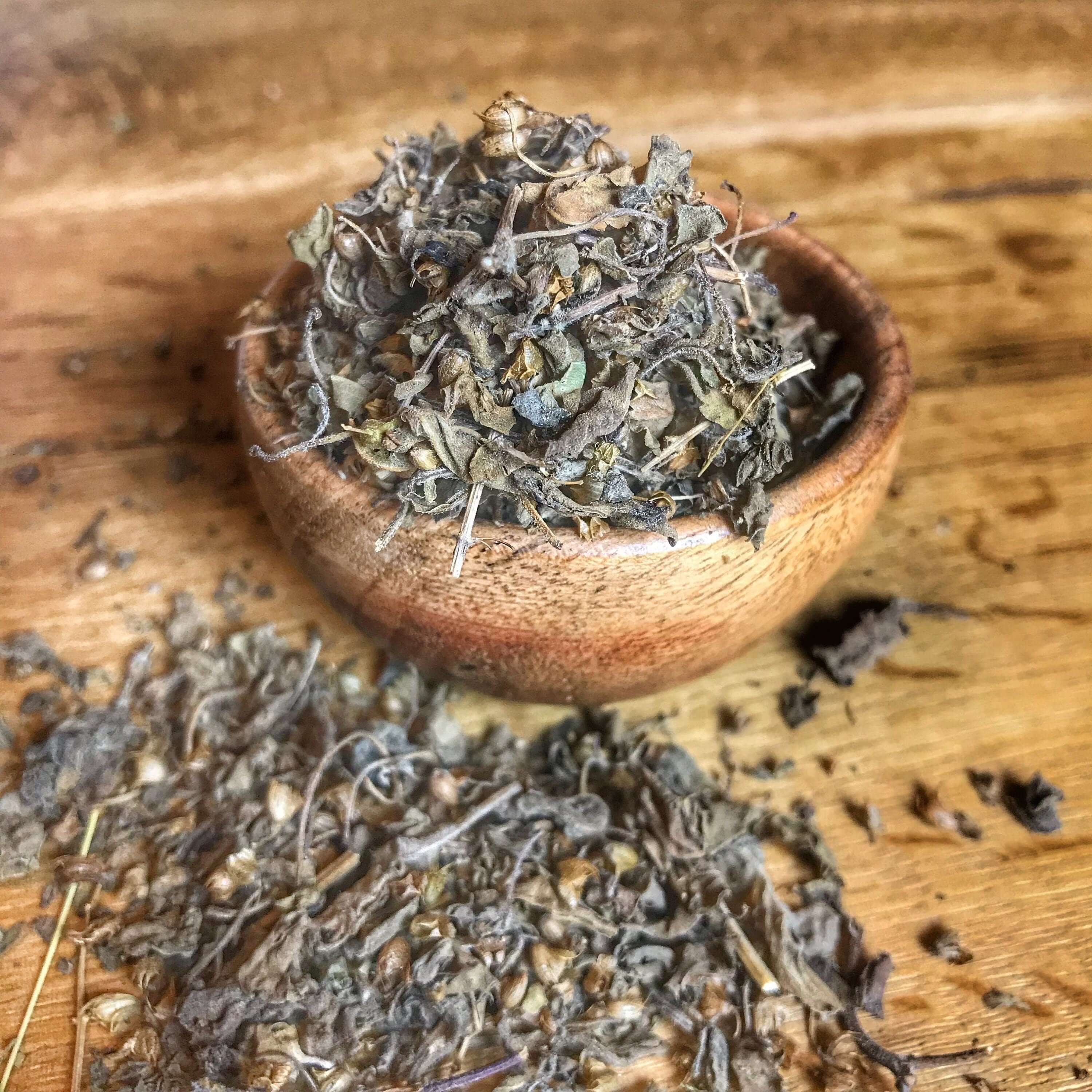 Top view of Sacred Plant Co premium Tulsi Herb, showcasing its dried texture and deep natural color on a wooden surface.