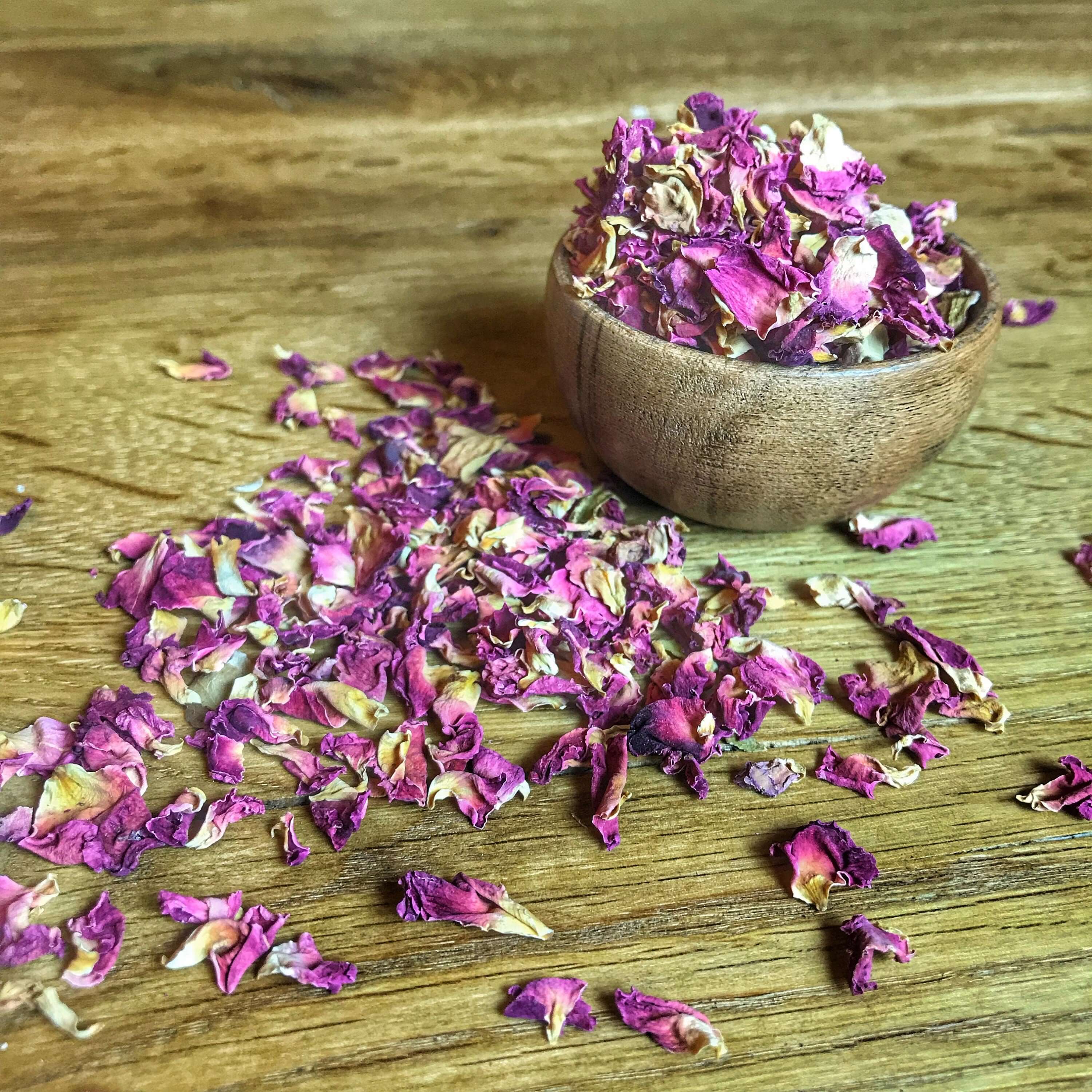 Premium Sacred Plant Co. dried Rose Petals, delicate rose petals spilling from a wooden bowl, showcasing their soft, velvety texture against a rustic wooden surface.
