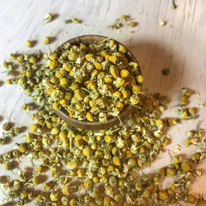Top view of a bowl full of dried chamomile flowers, showcasing the natural yellow hues and quality of the organic blossoms.