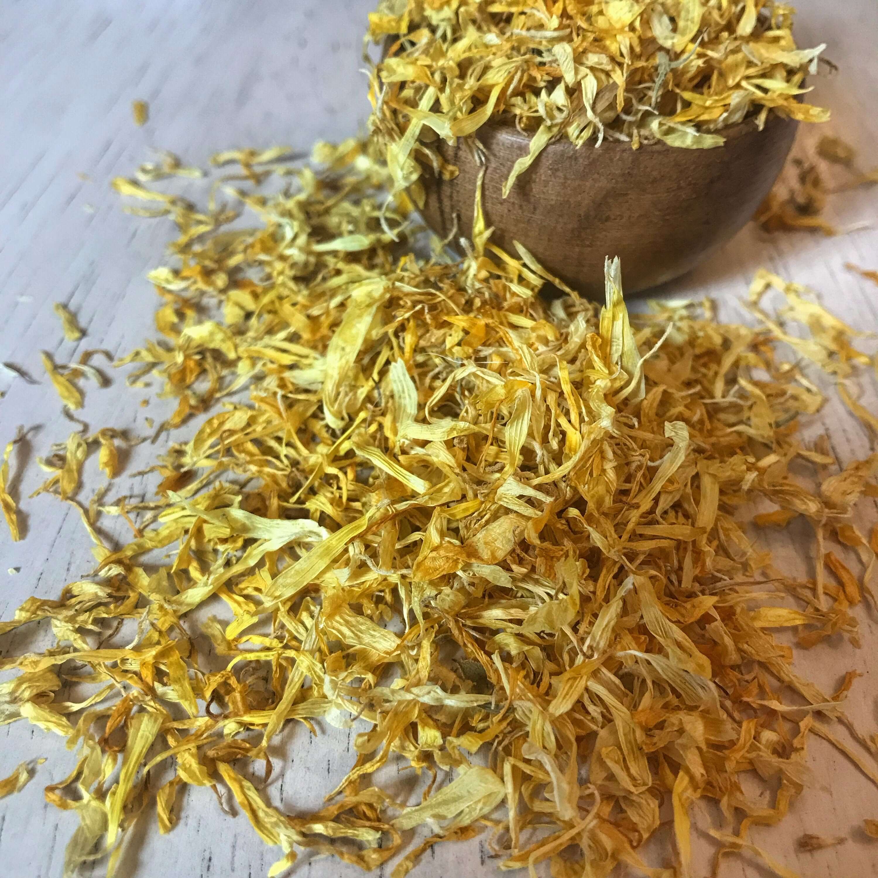 Sacred Plant Co dried Calendula Petals in a wooden bowl on a light surface, showcasing their vibrant yellow color and delicate texture.