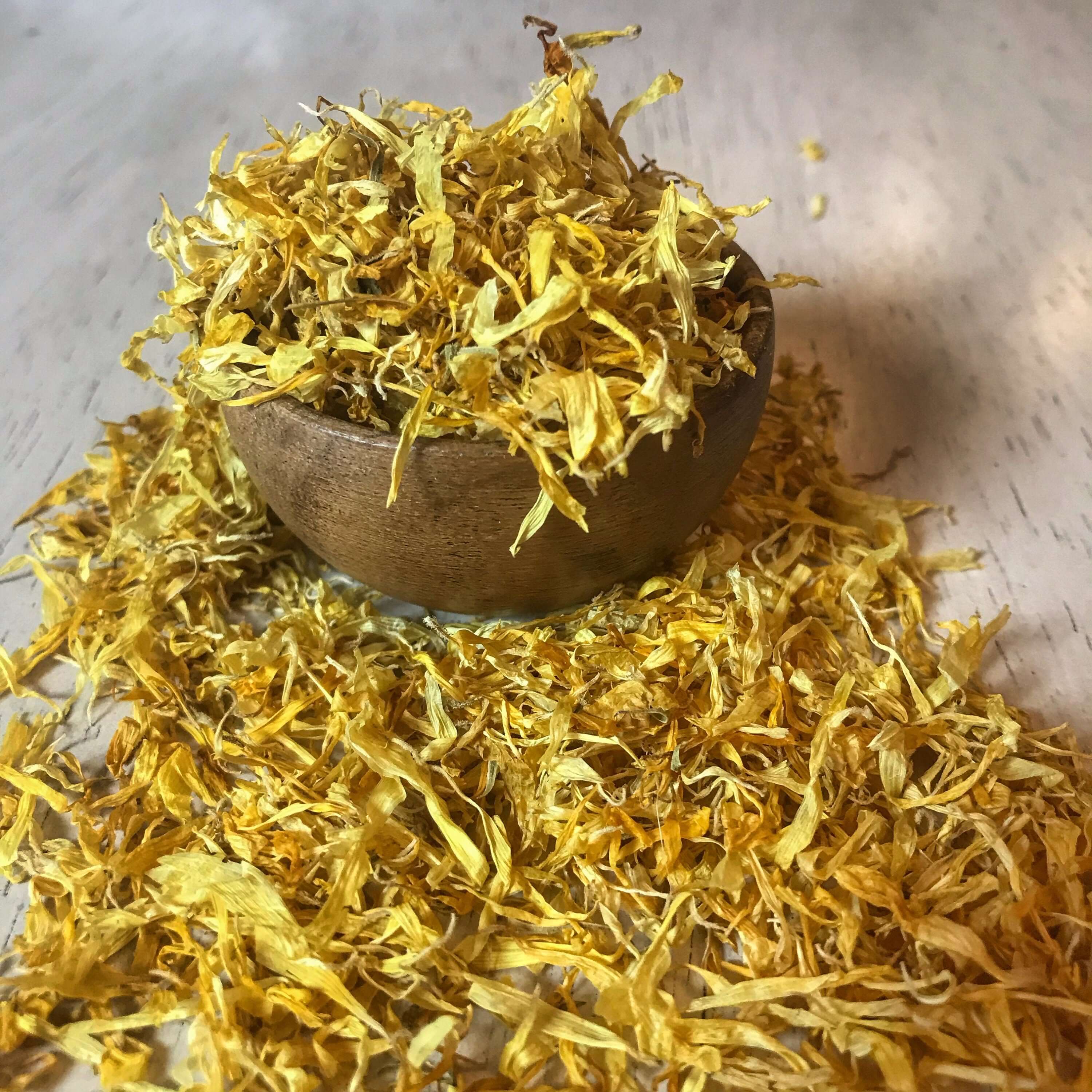Bright, golden Calendula Flowers scattered around a wooden bowl, emphasizing Sacred Plant Co’s premium herb quality.