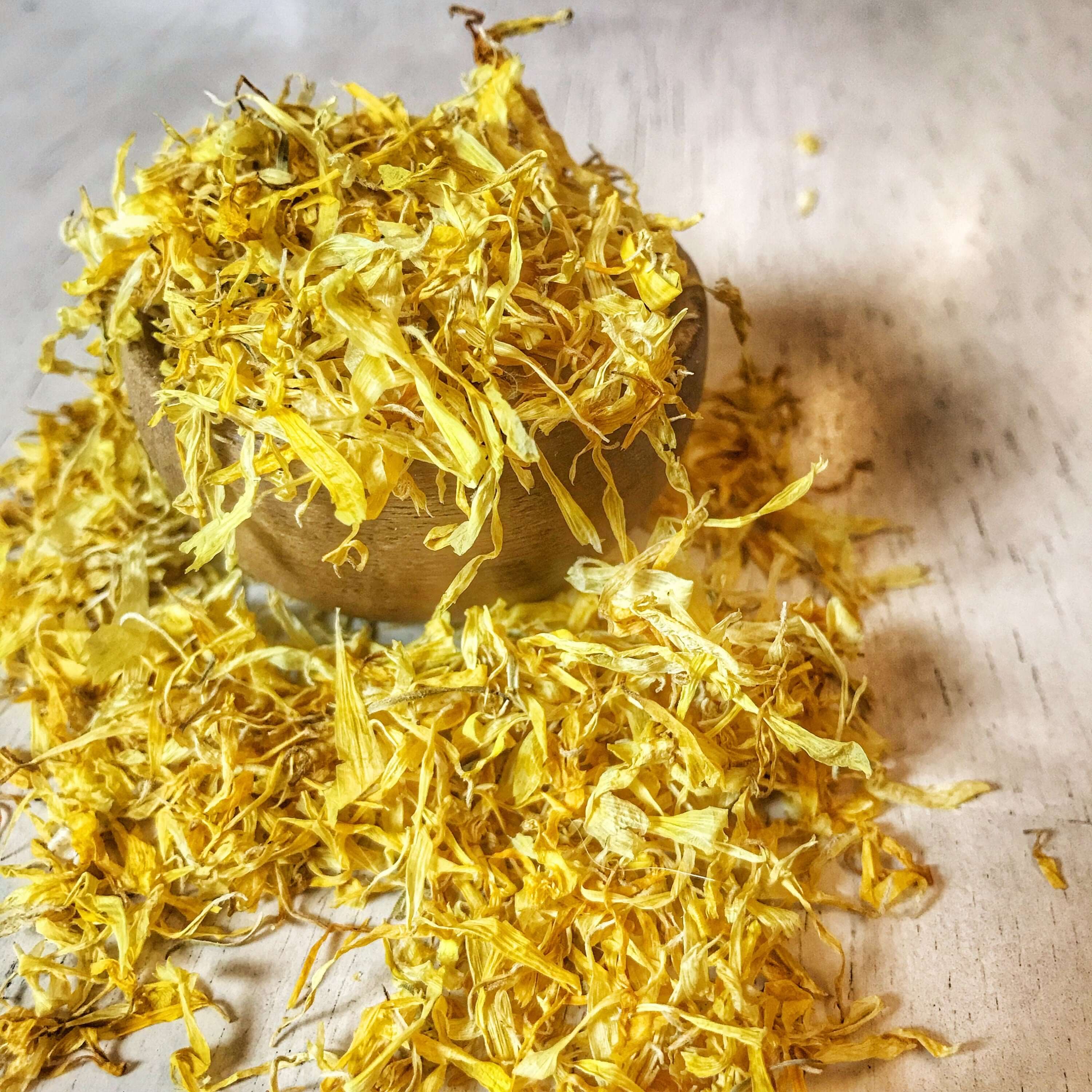Low-angle shot of premium-quality Calendula Petals of Sacred Plant Co, in a wooden bowl, beautifully lit to capture their bright yellow tones and fine details.