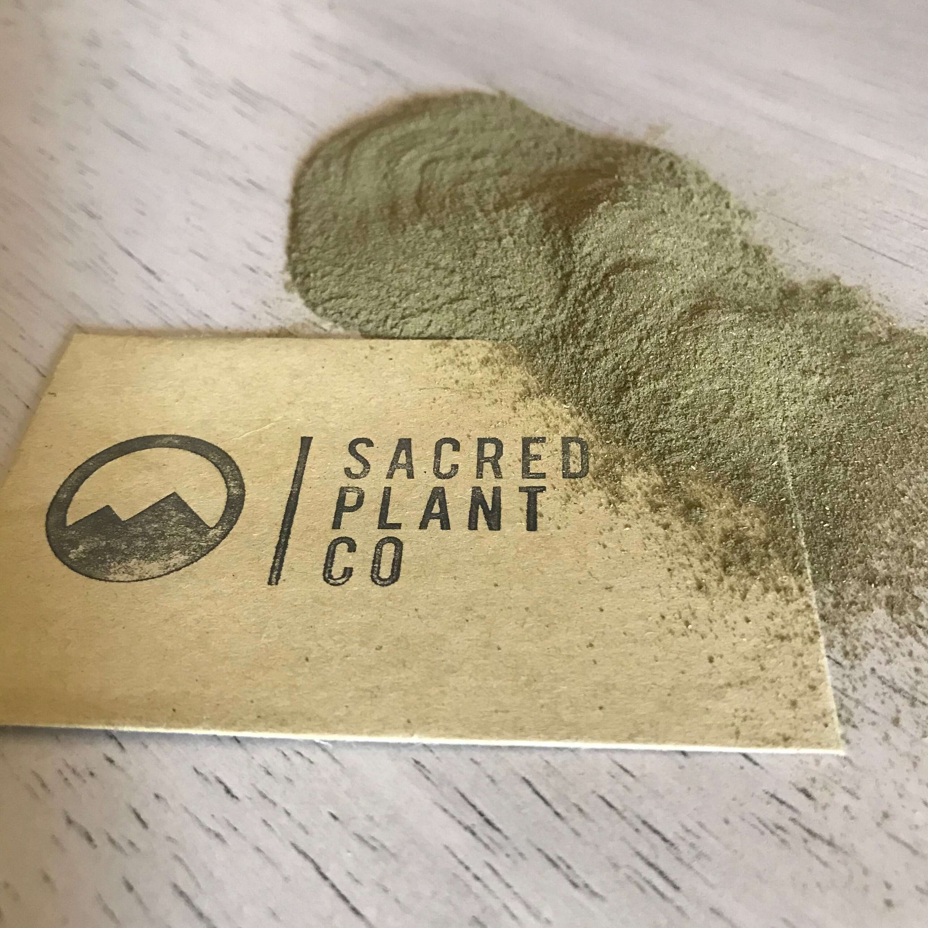 Finely textured Sacred Plant Co Neem Leaf Powder scattered, with an earthy green tone and kraft paper branding in the background.