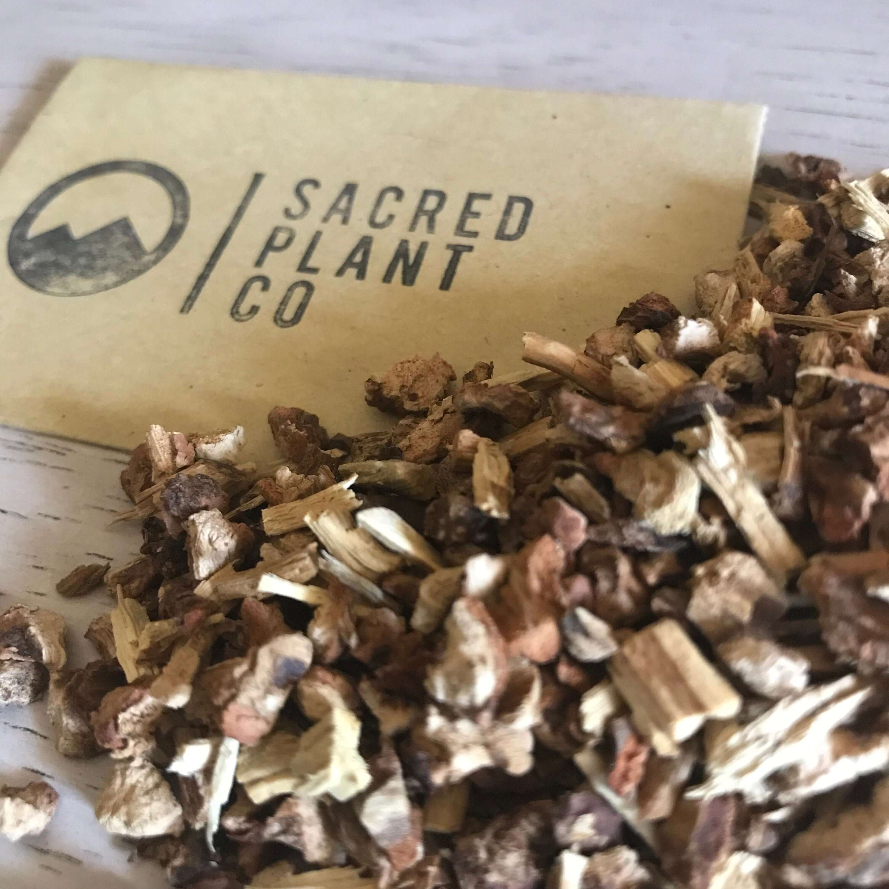 High-quality dried Sarsaparilla Root from Sacred Plant Co, rough-cut with natural beige and brown tones, placed on a smooth wood surface.