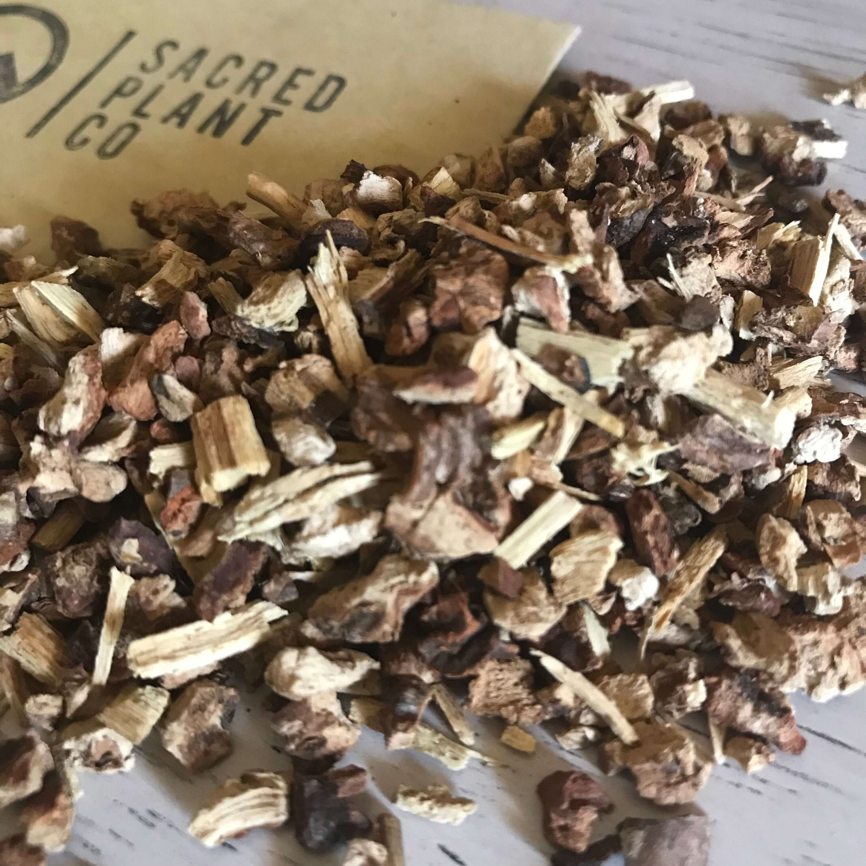 Rough-cut Sarsaparilla Root pieces, with earthy brown tones and a fibrous texture, displayed alongside Sacred Plant Co&