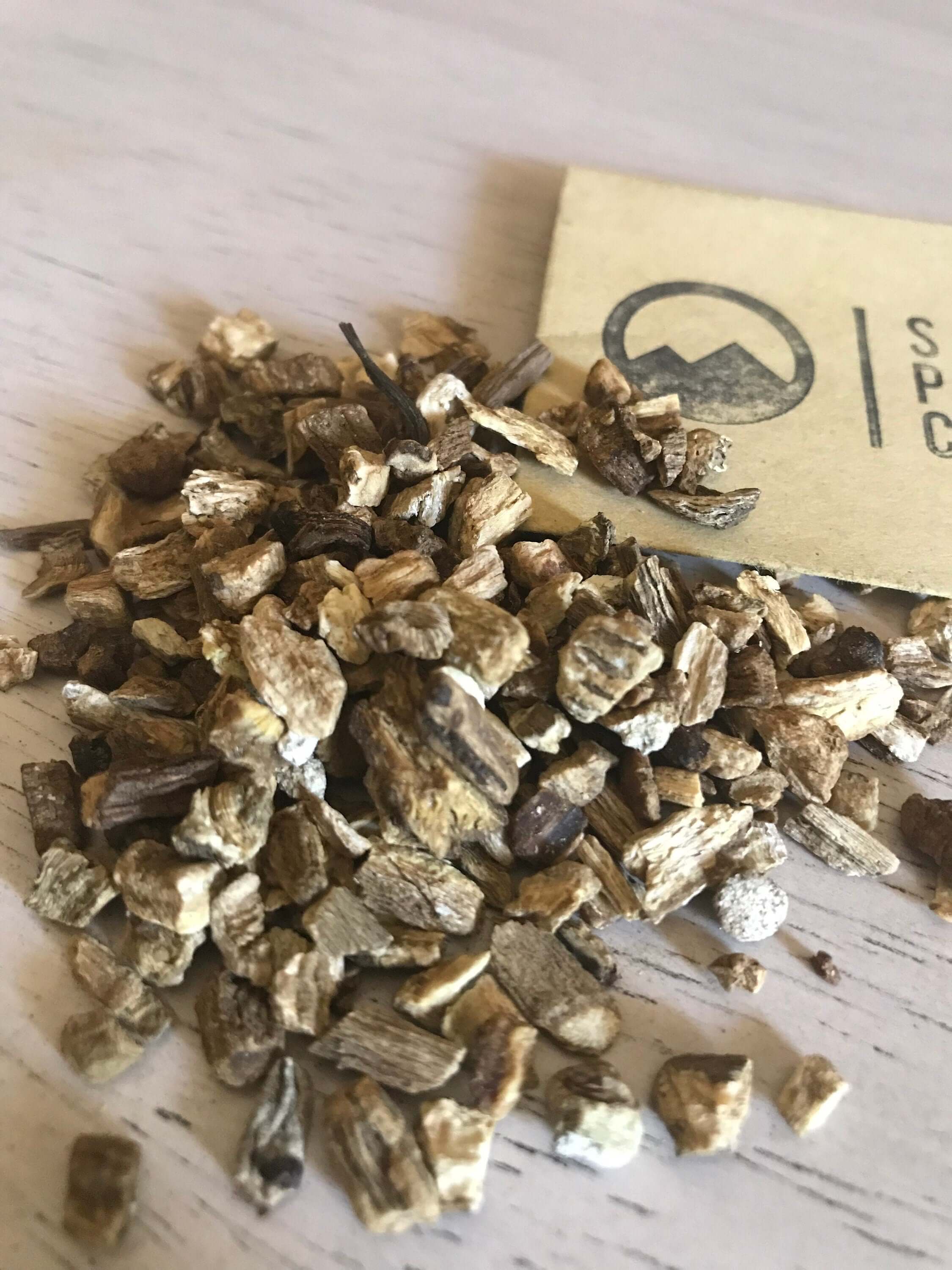 Angled shot of dried Burdock Root next to Sacred Plant Co packaging, showcasing premium natural herbs on a light surface.