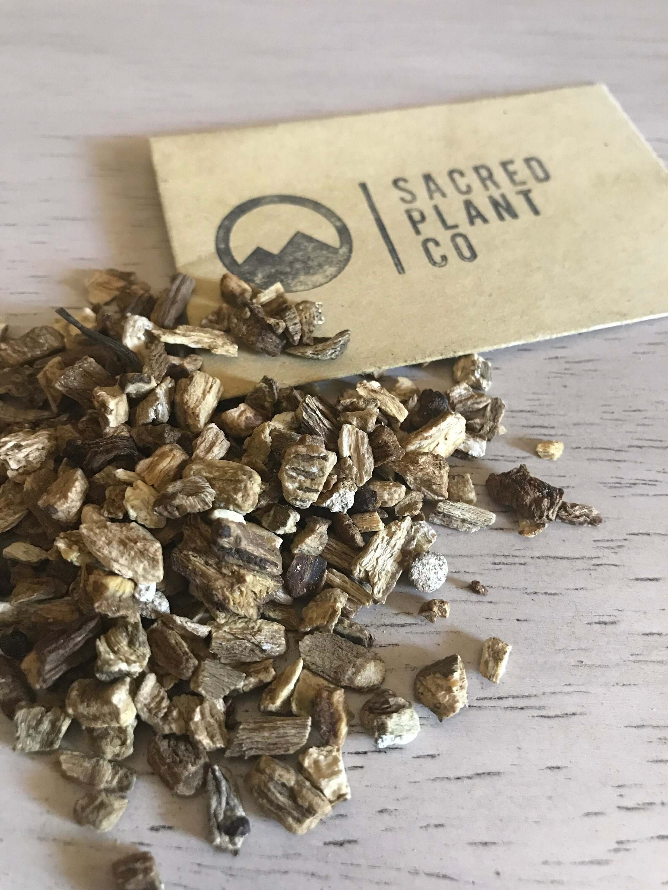 Dried Burdock Root positioned near Sacred Plant Co logo, captured at an angle to emphasize premium herbal quality.