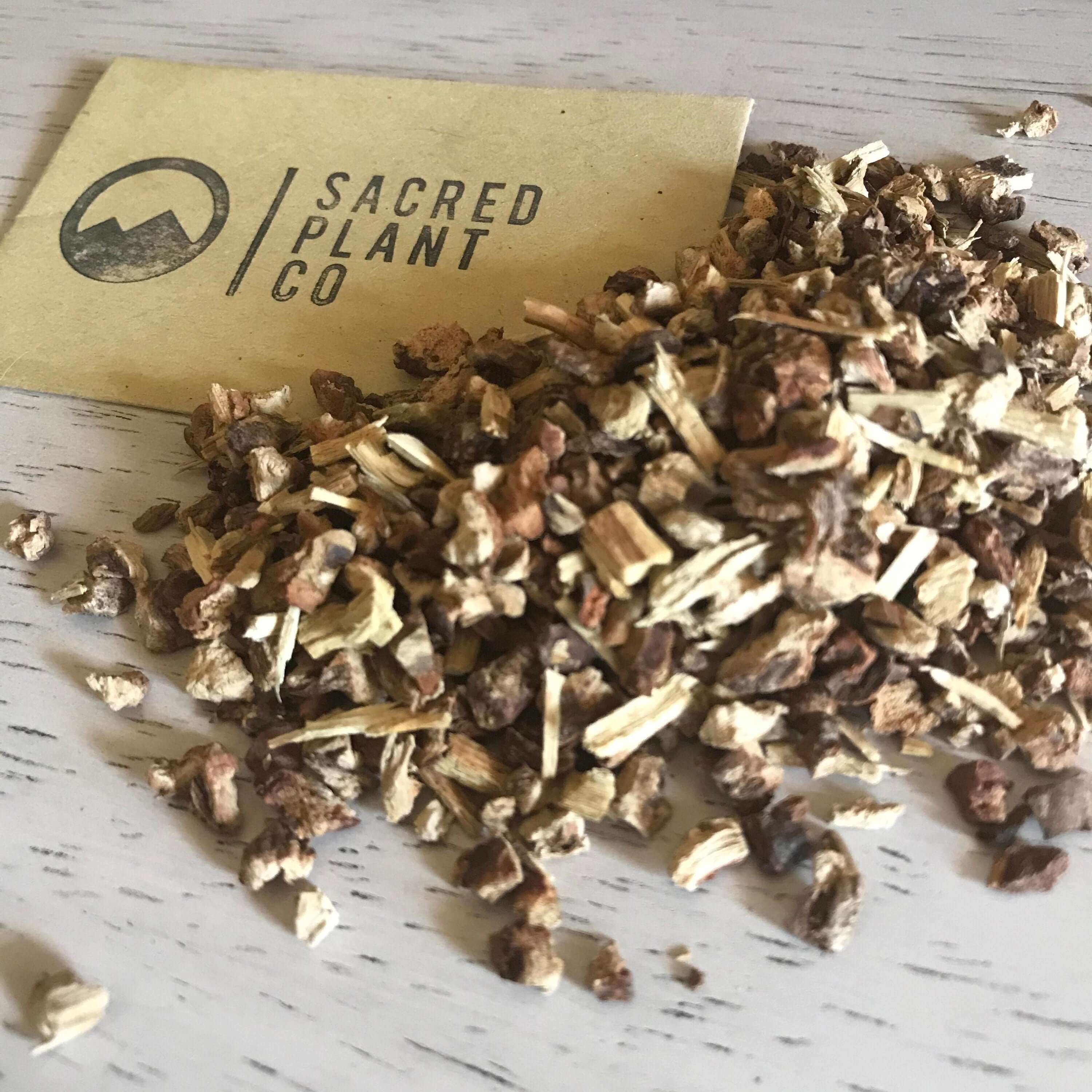 Premium dried Sarsaparilla Root from Sacred Plant Co, showcasing rough, earthy brown and beige tones on a light wood surface.