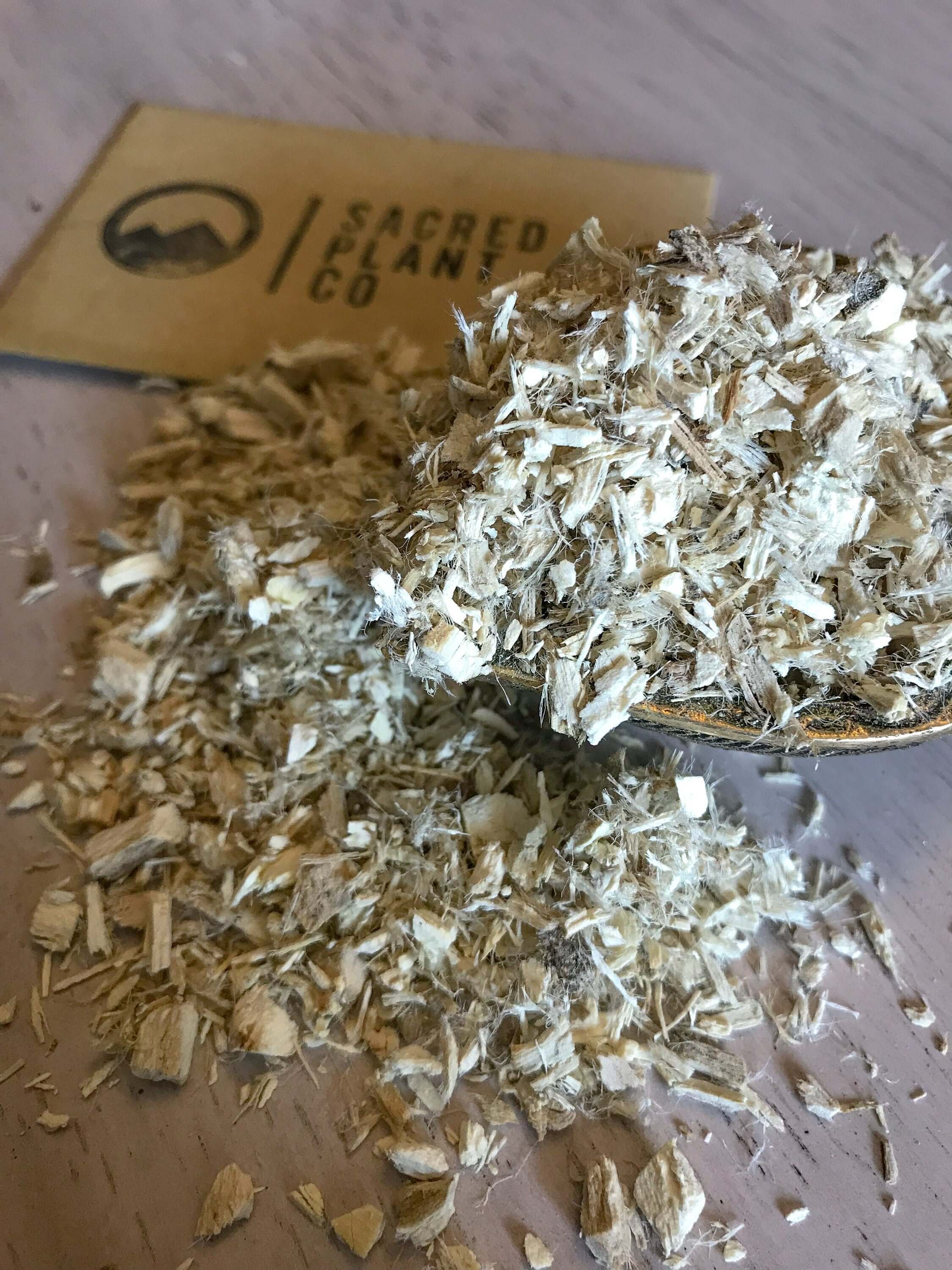 Close-up of freshly harvested Marshmallow Root on a wooden table, displaying its fine quality and organic texture with Sacred Plant Co label visible used for oil extraction.