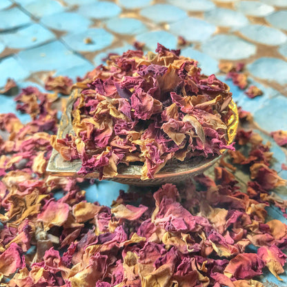 Artistically presented dried rose petals in a rustic bowl against a blue patterned background, ideal for homemade potpourri and bath soaks.