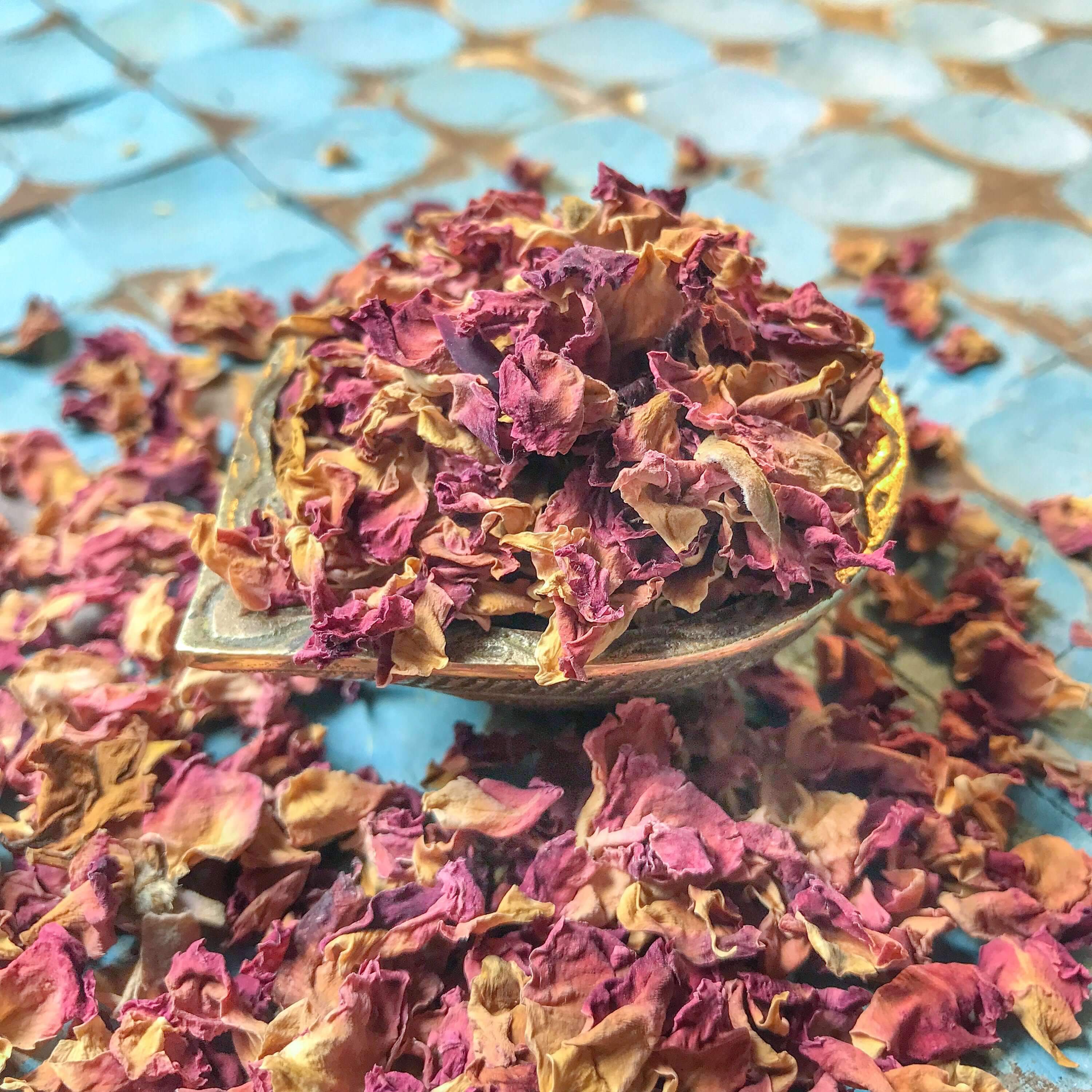Artistically presented dried Rose Petals in a rustic bowl against a blue patterned background, ideal for homemade potpourri and bath soaks.