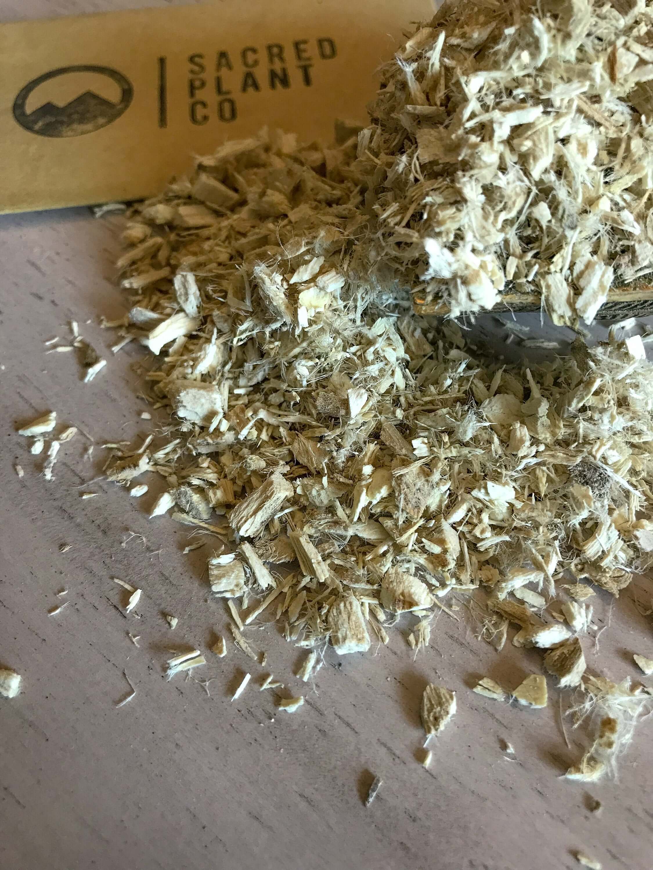 High-quality extracted Marshmallow Root with a fibrous, golden texture, set on a pale wood surface with Sacred Plant Co branding for a natural aesthetic.