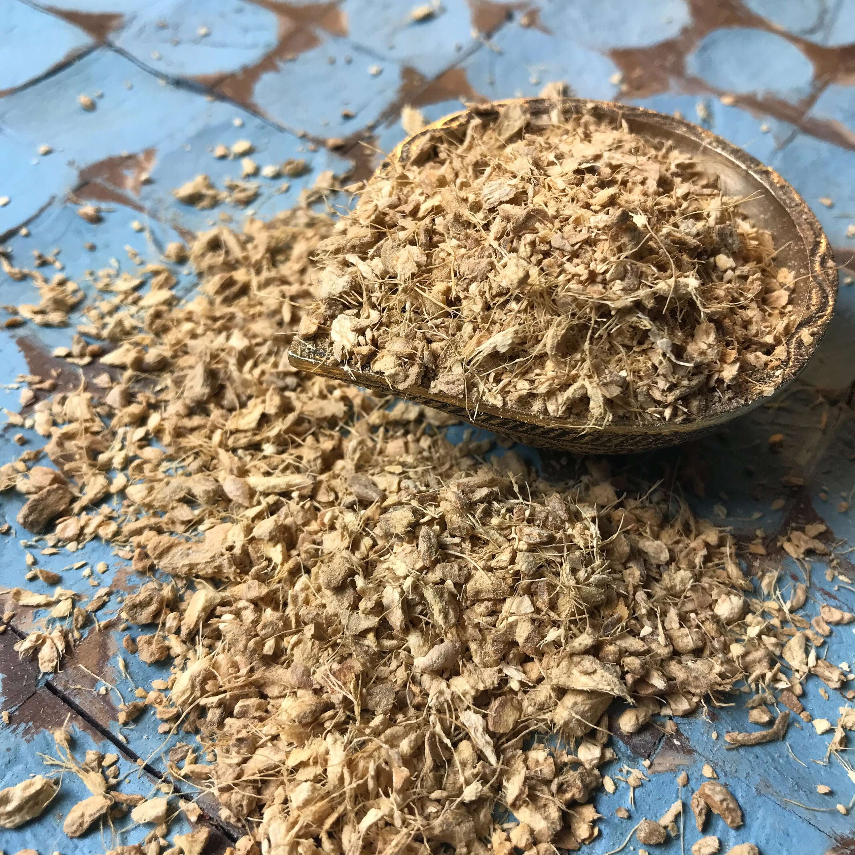 Finely shredded premium Ginger Root displayed on rustic blue tiles, emphasizing its rich texture and vibrant tones from Sacred Plant Co.
