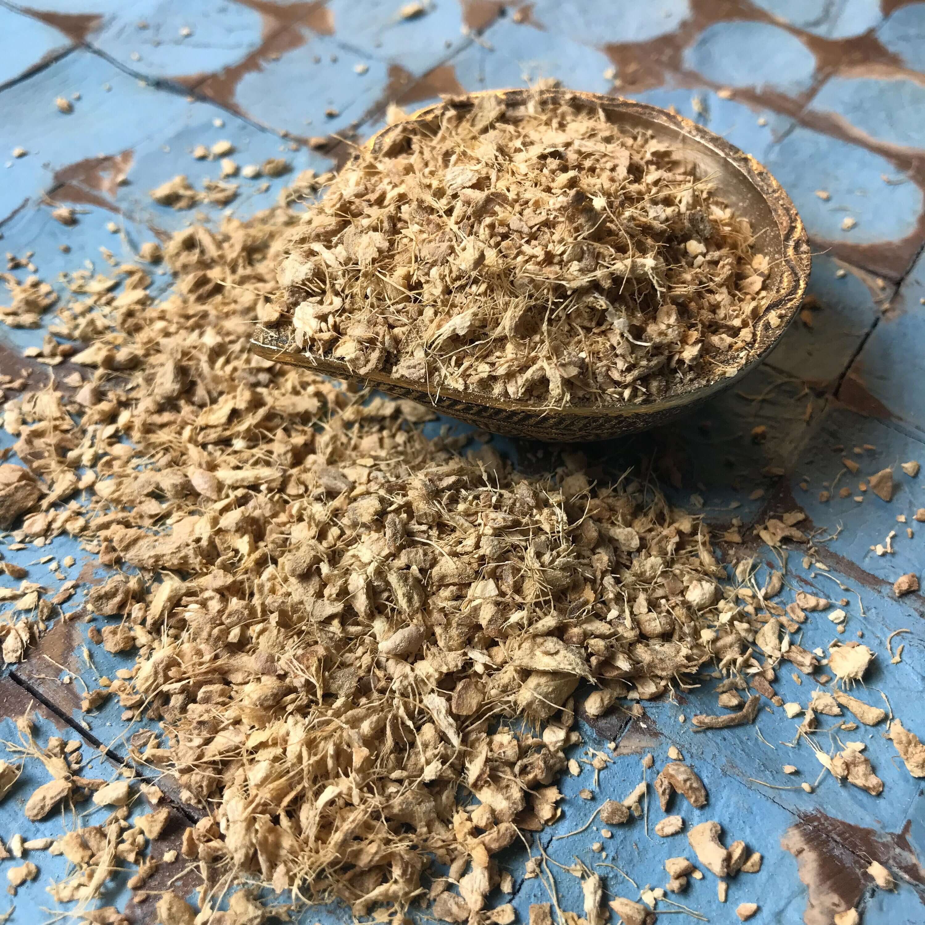 Premium Ginger Root crumbles spread on blue-patterned tiles, highlighting its natural texture and artisanal quality by Sacred Plant Co.