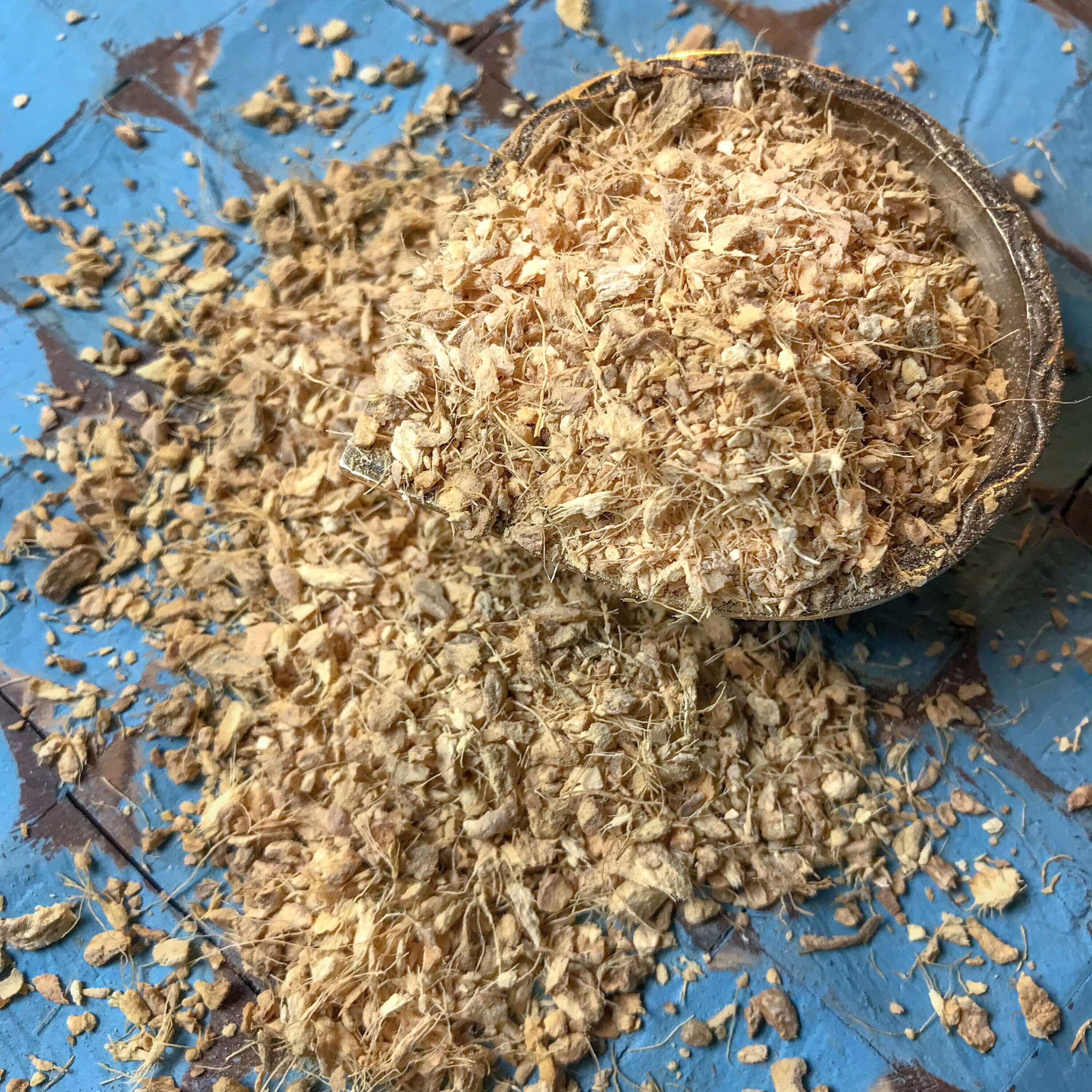 Natural Ginger Root shavings with rich golden hues on a textured blue surface, showcasing the premium quality of Sacred Plant Co’s herbs.