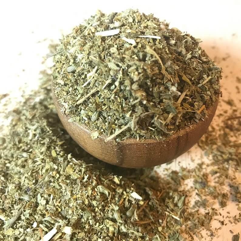 Top view of finely cut Damiana Herb, beautifully displayed on a light wood surface alongside a wooden bowl and Sacred Plant Co label.