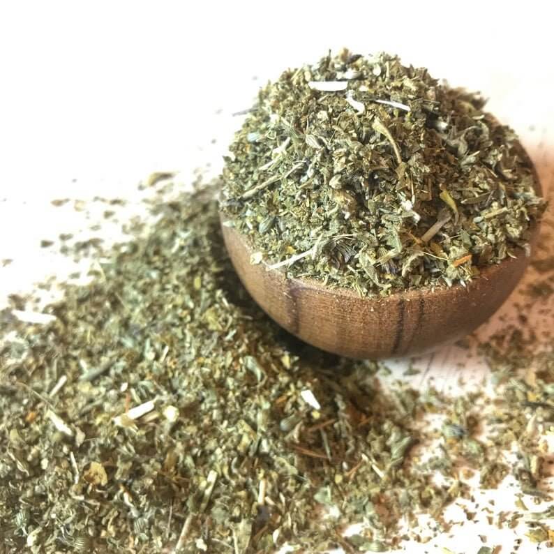 Organic Damiana Herb in a rustic wooden bowl, arranged on a natural wood background with scattered herb fragments at Sacred Plant Co.