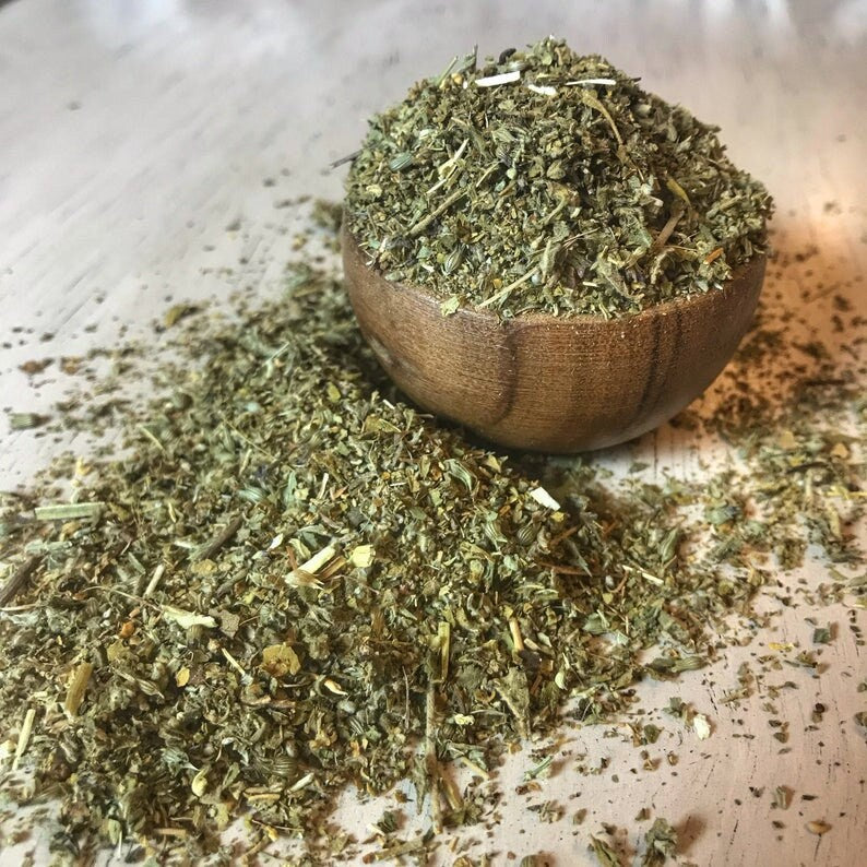 Close-up of soft, crushed Damiana Herb with subtle green hues, arranged in a wooden bowl on a smooth light wood surface, by Sacred Plant Co.