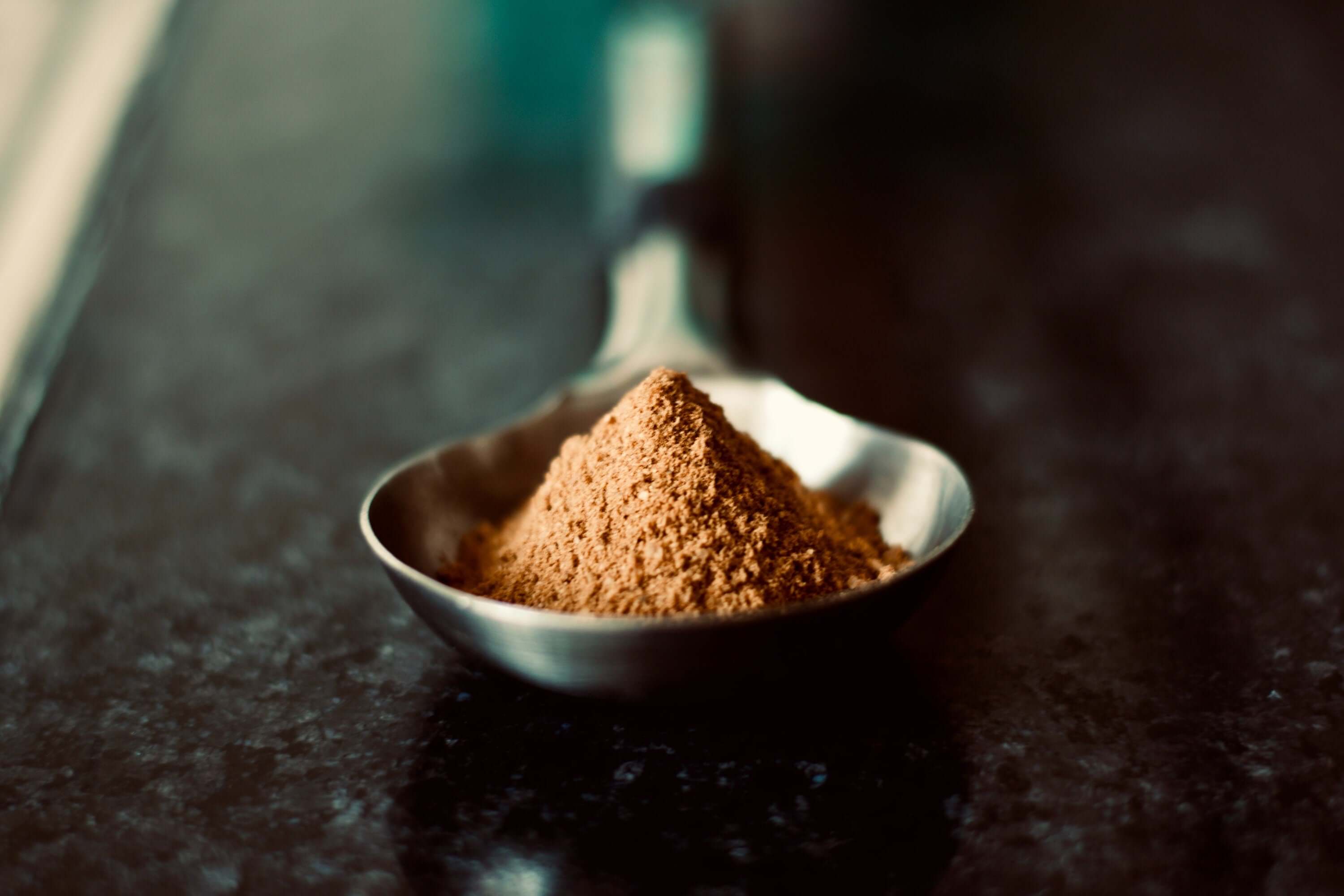 Raw Cacao Powder in a silver spoon on dark background, illustrating the fine texture and premium quality of Sacred Plant Co’s offering.