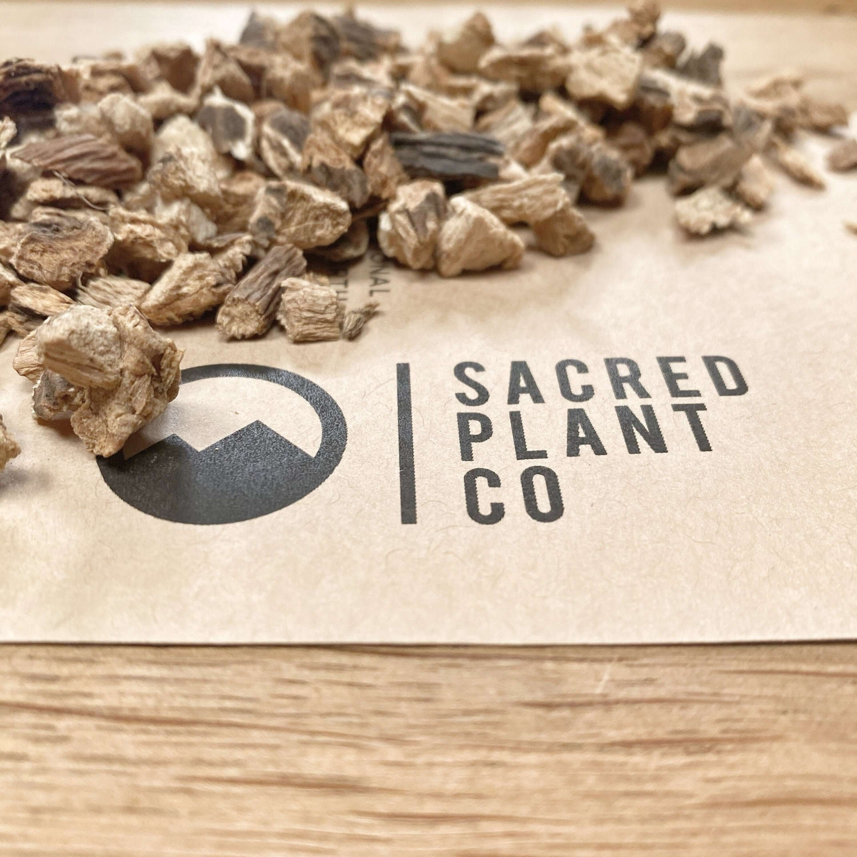 Premium quality Gentian Root pieces with rough texture, Sacred Plant Co logo in view, set against a warm, natural wood background.